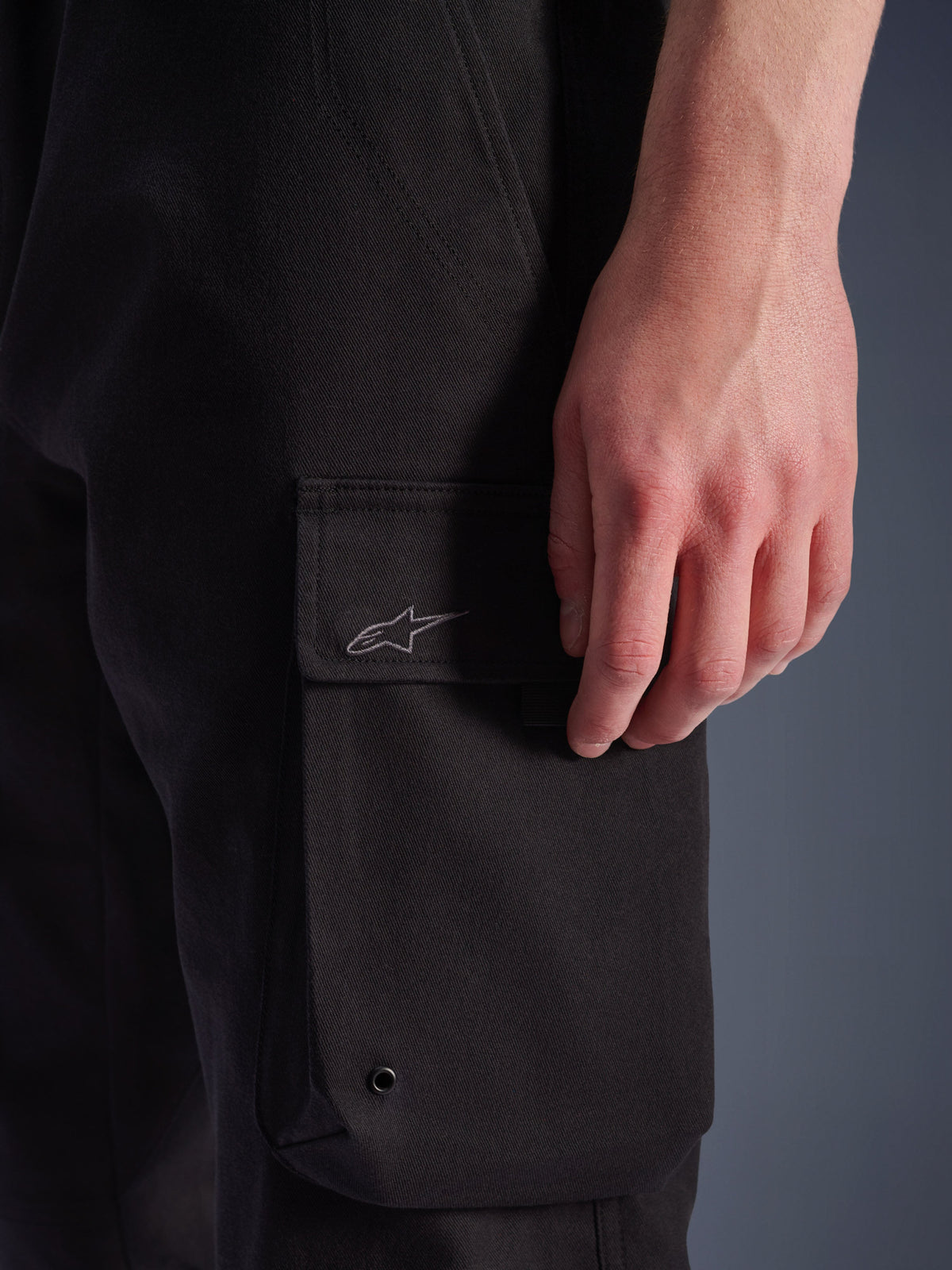 Alpinestars Flex-AST Cargo-bukser, urbane motorcykelbukser, sort, nærbillede af cargolomme på siden med broderet Astar-logo, metaløje og slidstærk stretch-twill-tekstur