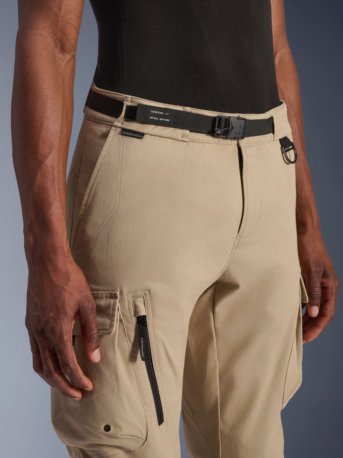 Alpinestars Flex-AST Cargo bukser - Short, lys beige, nærbillede af talje og lår, med sort justerbart bælte med Alpinestars-branding, metal D-ring og funktionelle cargolommer med lynlåse og klapper med trykknapper, urbant moderne motorcykeludstyr