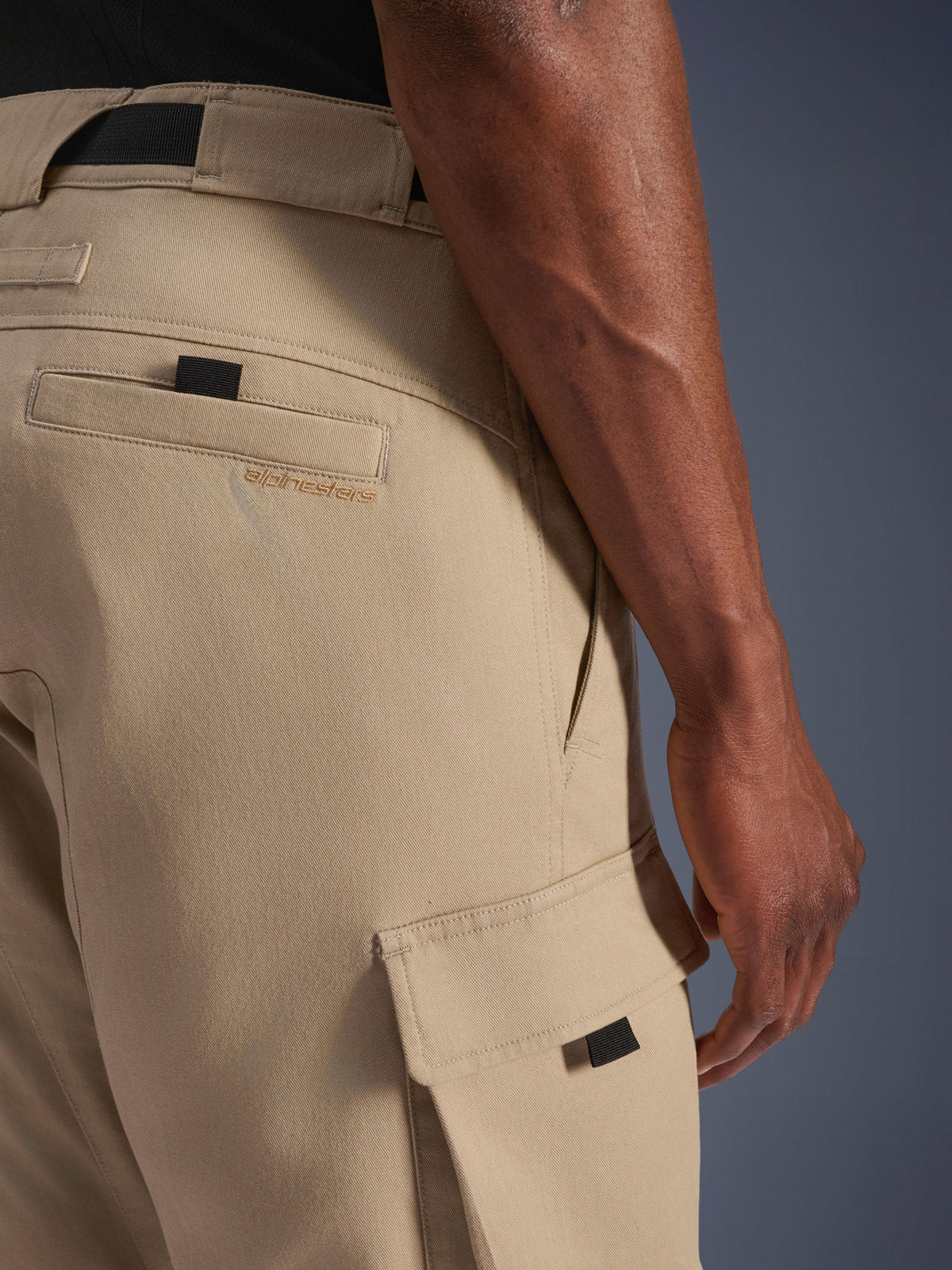 Alpinestars Flex-AST Cargo Bukser - Short, lysebeige, nærbillede fra siden, der viser cargolomme med sort trækstrop og broderet logo på baglommen, slidstærkt tekstilmateriale, urbant motorcykeludstyr.