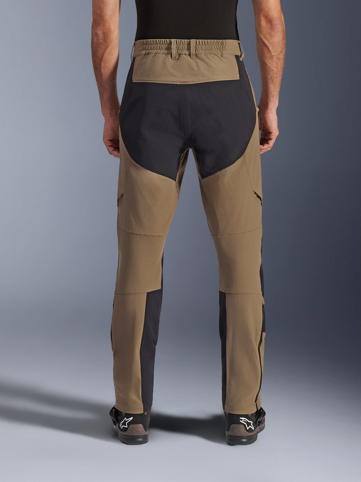 Alpinestars Flex-AST Explorer Pants, Adventure Motorcycle Pants, Walnut Black, rear view worn by rider, black ripstop reinforcement panels on the seat and inner legs, elasticated waistband, long lower leg zippers, and matching adventure boots