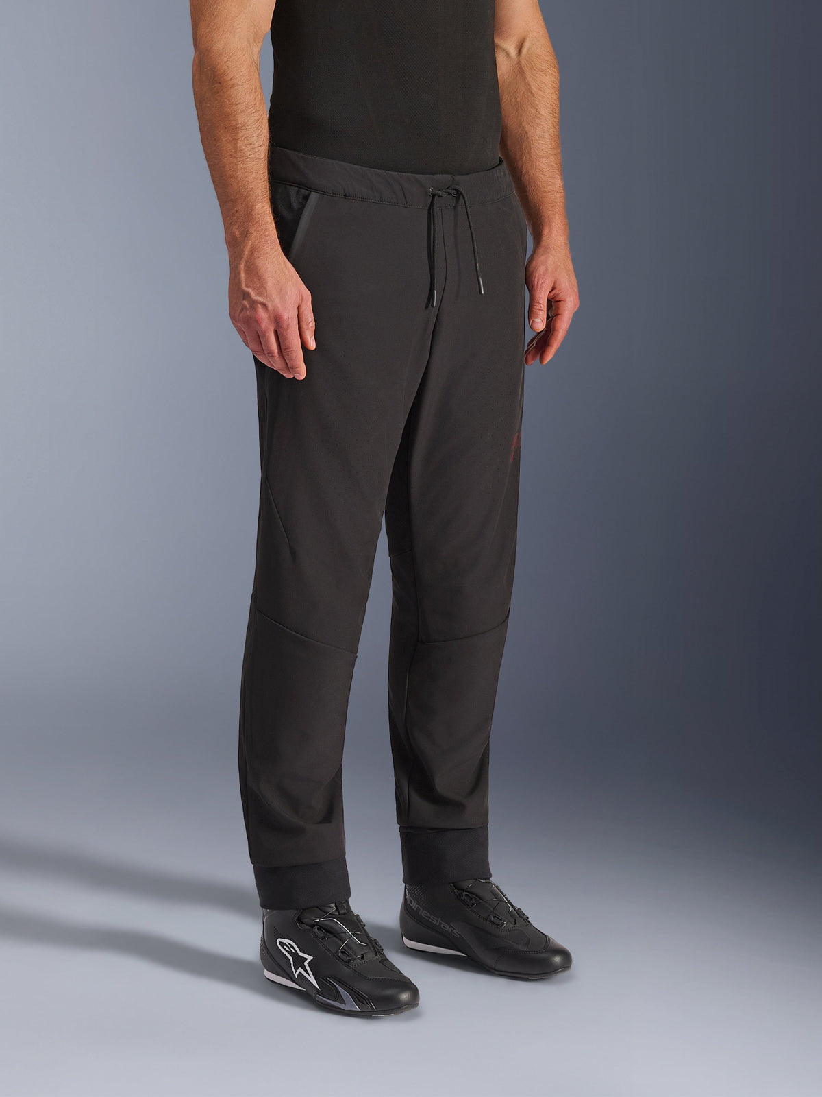 Alpinestars Aeroshell Airflow bukser, sorte motorcykelbukser, båret af model med sorte køresko, med snøre i taljen, ankelmanchetter og laserperforeret softshell-materiale for maksimal ventilation