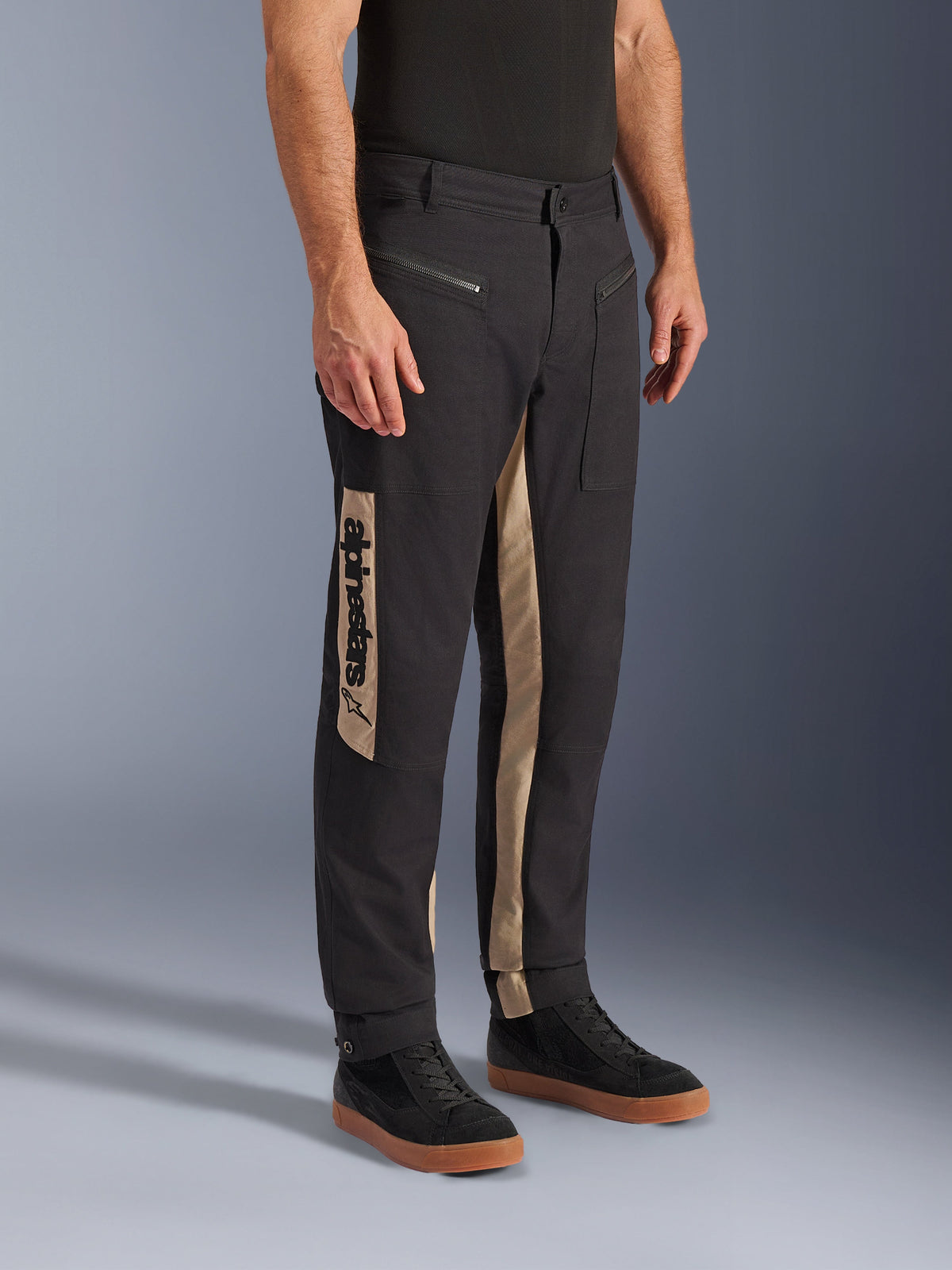 Alpinestars Flex-AST Canvas bukser, urbane motorcykelbukser, Black Aluminum, med sandfarvede sidepaneler og et lodret Alpinestars-logo, arbejdstøjsinspireret design med lynlåslommer og ergonomisk snit, båret med afslappede sorte sneakers for et moderne bylook.