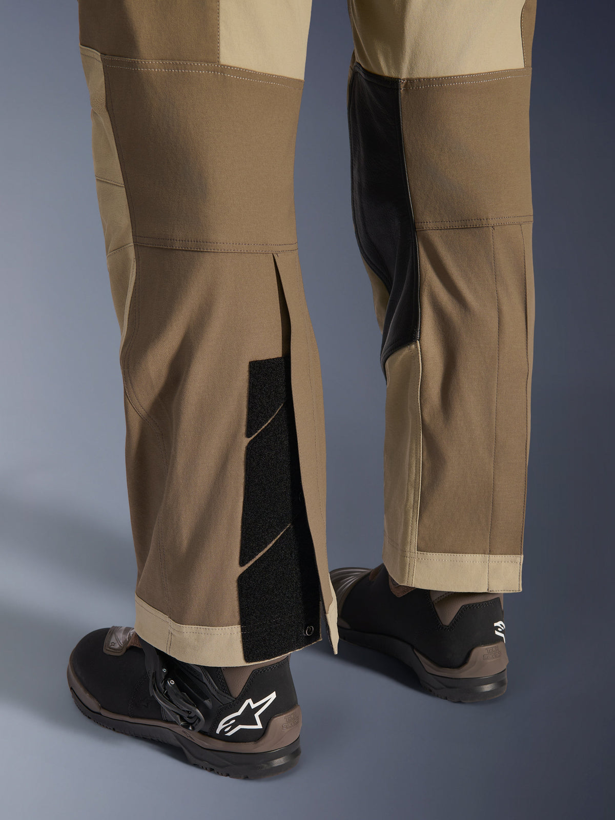 Alpinestars Maxdura Dual bukser i Walnut Aluminum, detaljeret visning af underbenet og sømmen med over-støvle-design, justerbare burrelukninger og forstærkede inderpaneler, kombineret med sorte motorcykelstøvler.