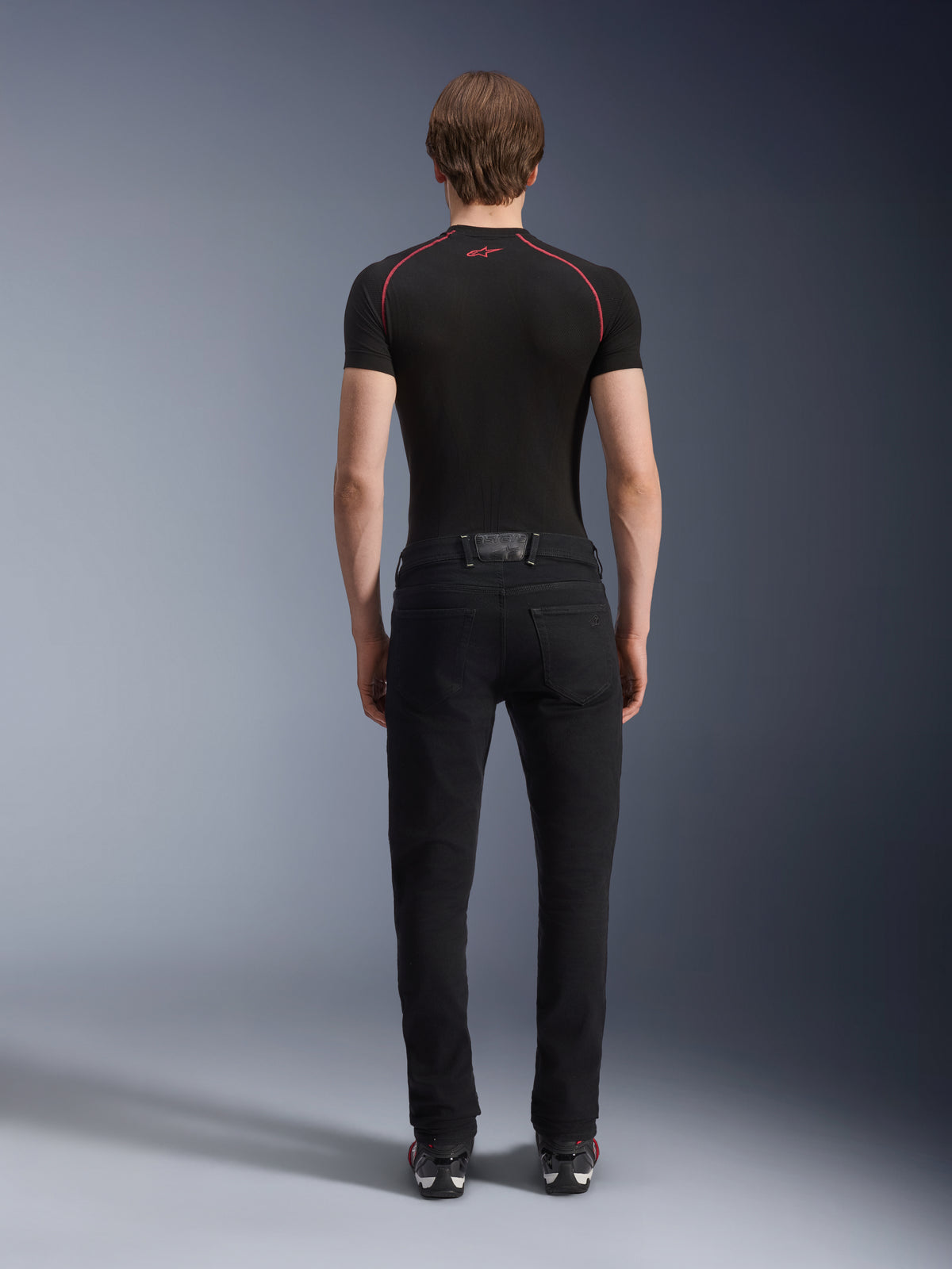 Alpinestars Copper V3 Denim bukser i Black Rinse, set bagfra på en model, regulære motorcykeljeans med lige ben i strækdenim, kombineret med en sort kortærmet kompressionsbluse og køresko, urbant køreudstyr