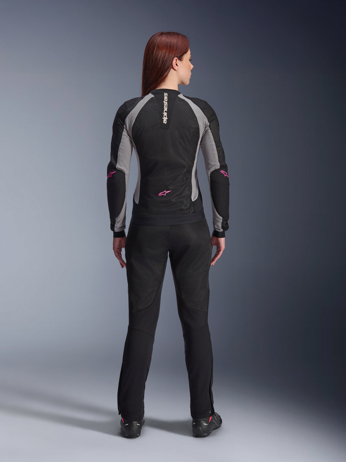 Stella Troop-Air-jakke til kvinder og matchende bukser set bagfra, Black Ash Gray og Pink Fluo, letvægts mesh-motorcykeludstyr med grå paneler og pink fluo-detaljer, med lodret Alpinestars-branding og stjernelogoer.