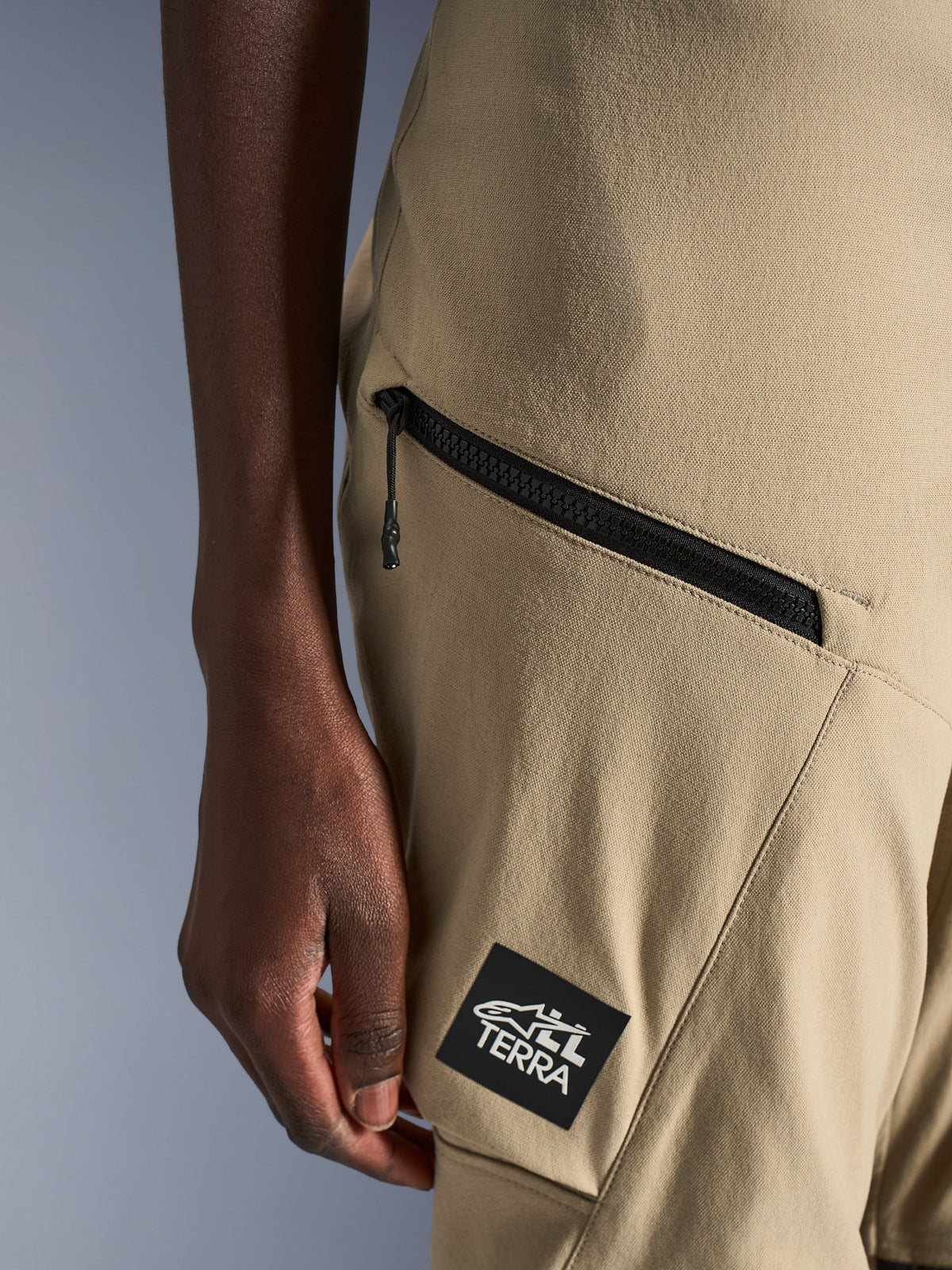 Alpinestars Stella Flex-AST Explorer Pants, Women's Motorcycle Pants, Sand, close-up detail of zippered cargo pocket and black ALL TERRA logo patch, durable ripstop textile construction for adventure touring