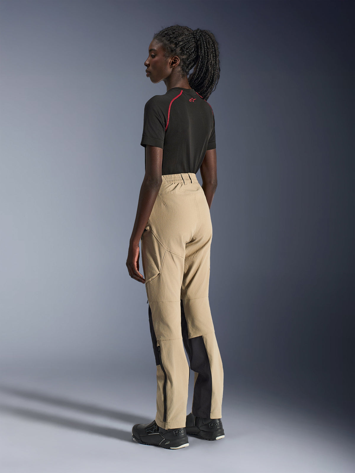 Alpinestars Stella Flex-AST Explorer Pants, Women's Motorcycle Pants, Sand and Black, featuring a side-back view on a model, paired with a black t-shirt and riding boots, highlights ripstop reinforcements and zippered lower leg openings.