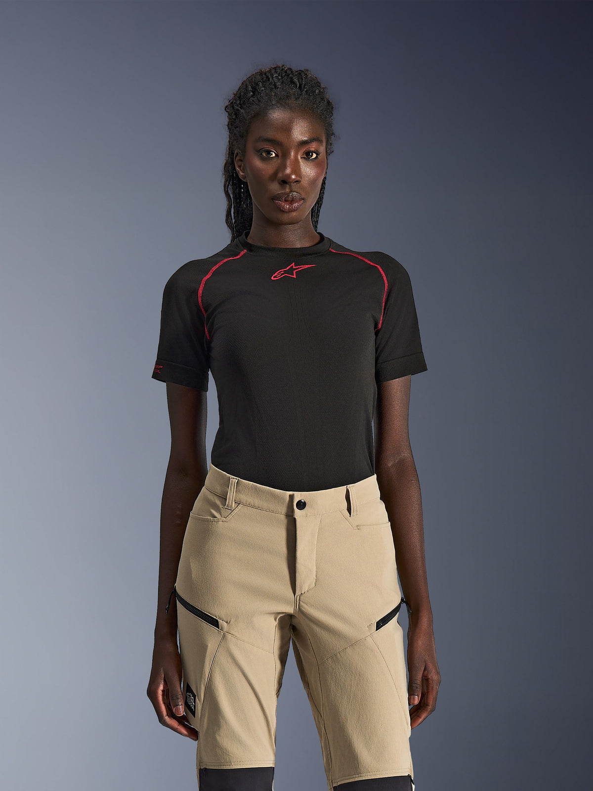 Alpinestars Stella Flex-AST Explorer Pants, Women's motorcycle pants in Sand, worn with a black technical short-sleeve top with red stitching, adventure touring gear featuring zippered cargo pockets and durable ripstop fabric.