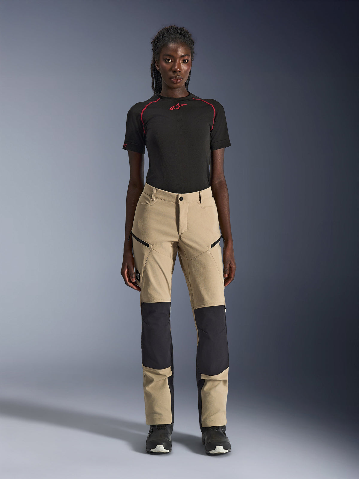 Alpinestars Woman Stella Flex-AST Explorer Pants, Women's Motorcycle Pants, Tan with black panels, worn by a model with a black short-sleeved top and black boots, featuring reinforced knee panels, zippered cargo pockets, and breathable ripstop fabric for warm-weather adventure riding.