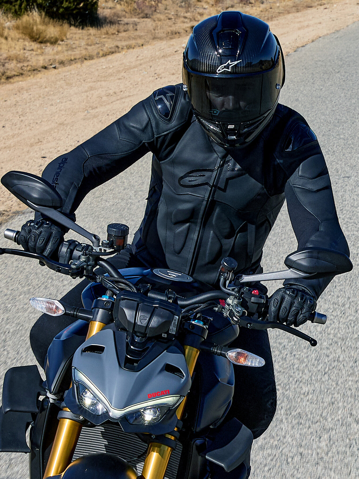 Alpinestars Dusk læderjakke til herrer, sort road racing-jakke med skulderslidere, på en grå Ducati.