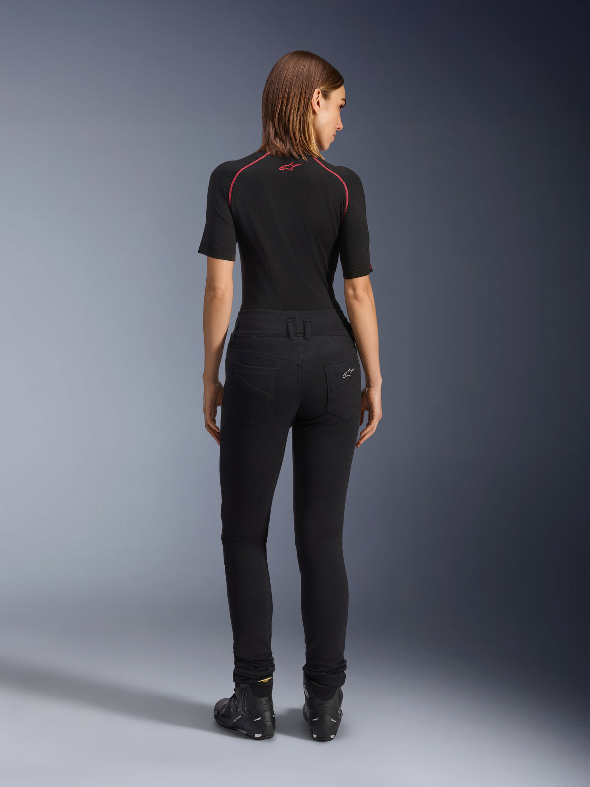 Alpinestars Banshee Leggings til damer, sorte motorcykel leggings, set bagfra som viser den figursyede pasform og det anatomiske strækstof, med baglommer og logodetalje, båret med et sort baselayer og køresko, urbant motorcykeludstyr til kvinder