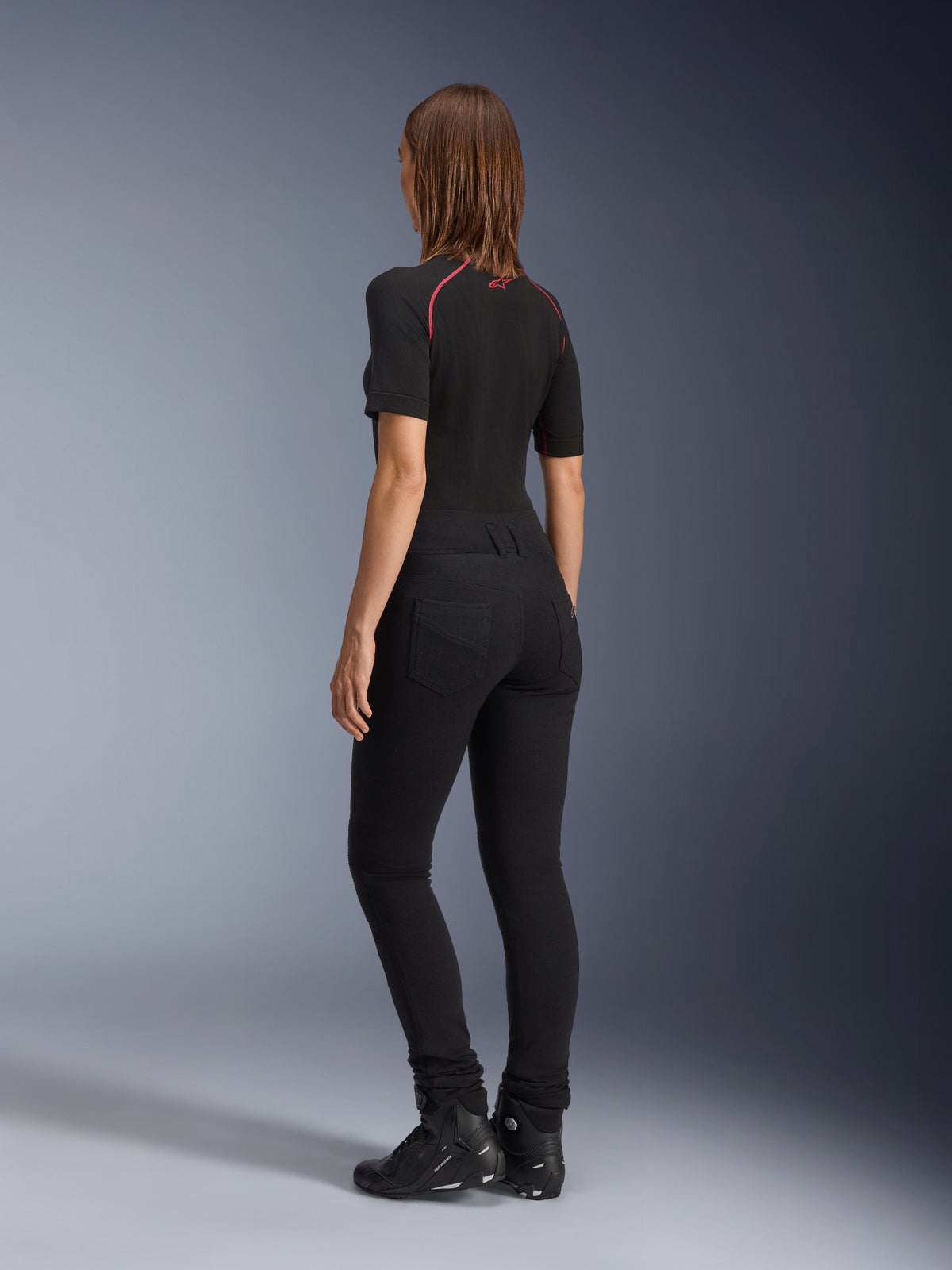 Alpinestars Banshee Leggings til kvinder, sort, set bagfra med tætsiddende anatomisk strækpasform og baglommer, båret med en sort kortærmet top og motorcykelstøvler, stilfuldt urbant motorcykeludstyr til kvinder