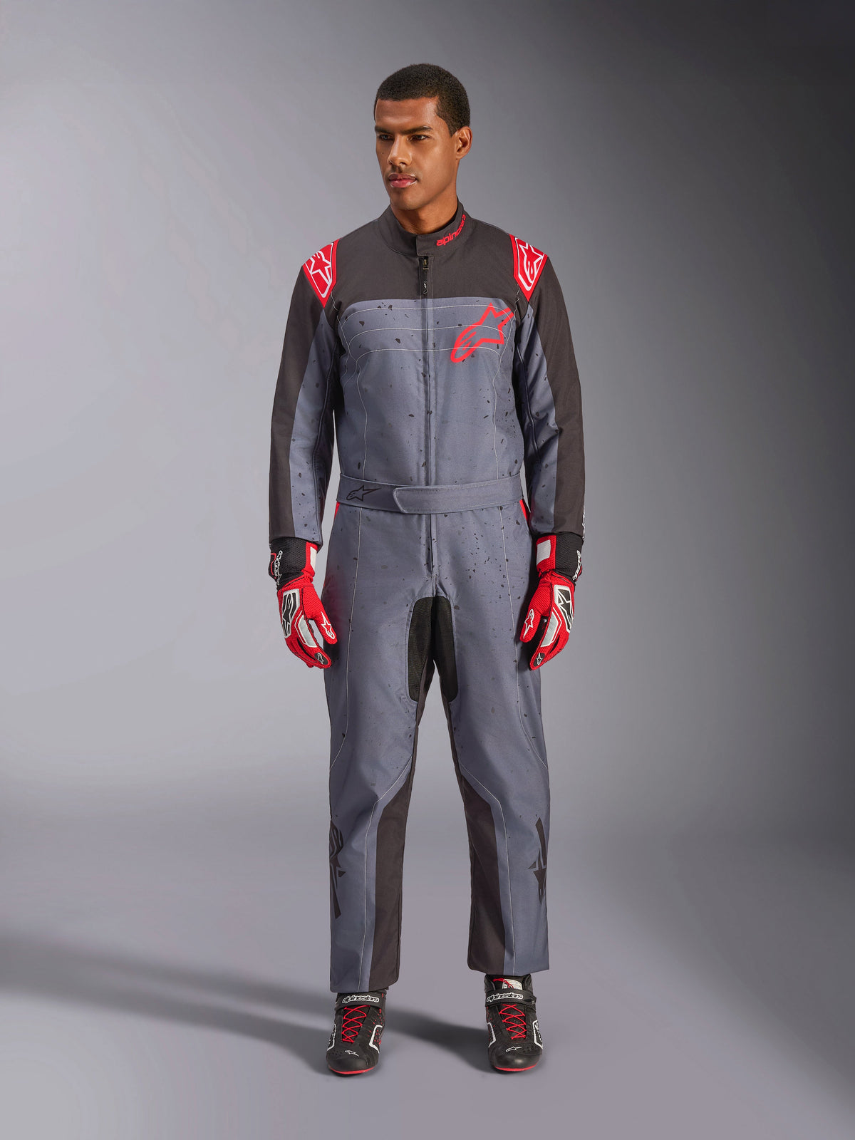 Alpinestars KMX-9 V3 Graphic 6 Suit, Karting Suit, Anthracite Black and Red, gray speckled graphic pattern, black panels on inner arms and legs, red Alpinestars logos on shoulders and chest, worn with red racing gloves and black shoes