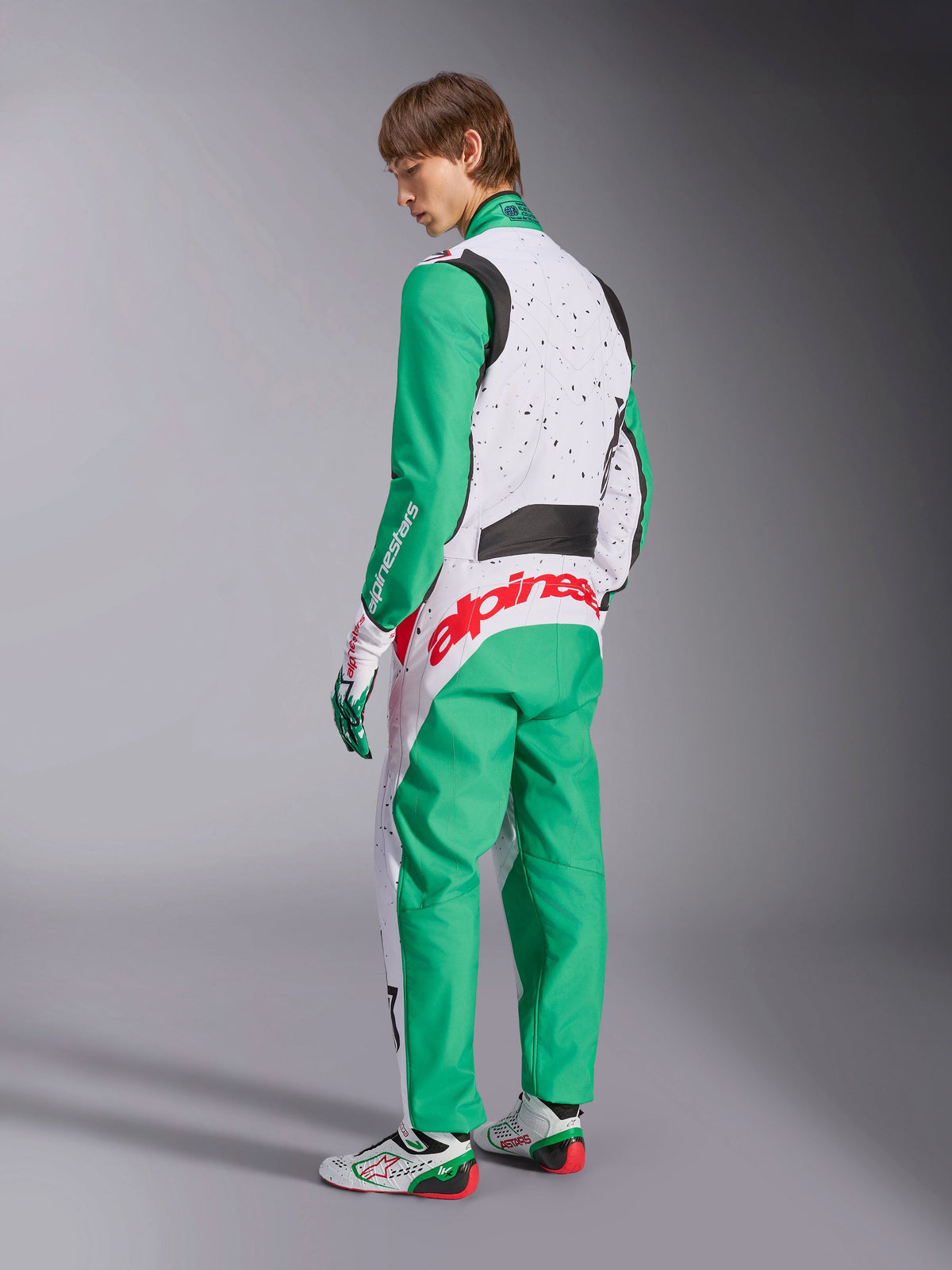 Alpinestars KMX-9 V3 Graphic 6 Suit, Karting Suit, White Green and Red, model viewed from the back-side, featuring green sleeves and lower panels, white upper torso with black speckle detail, bold red Alpinestars branding across the lower back, paired with matching white and green karting shoes.