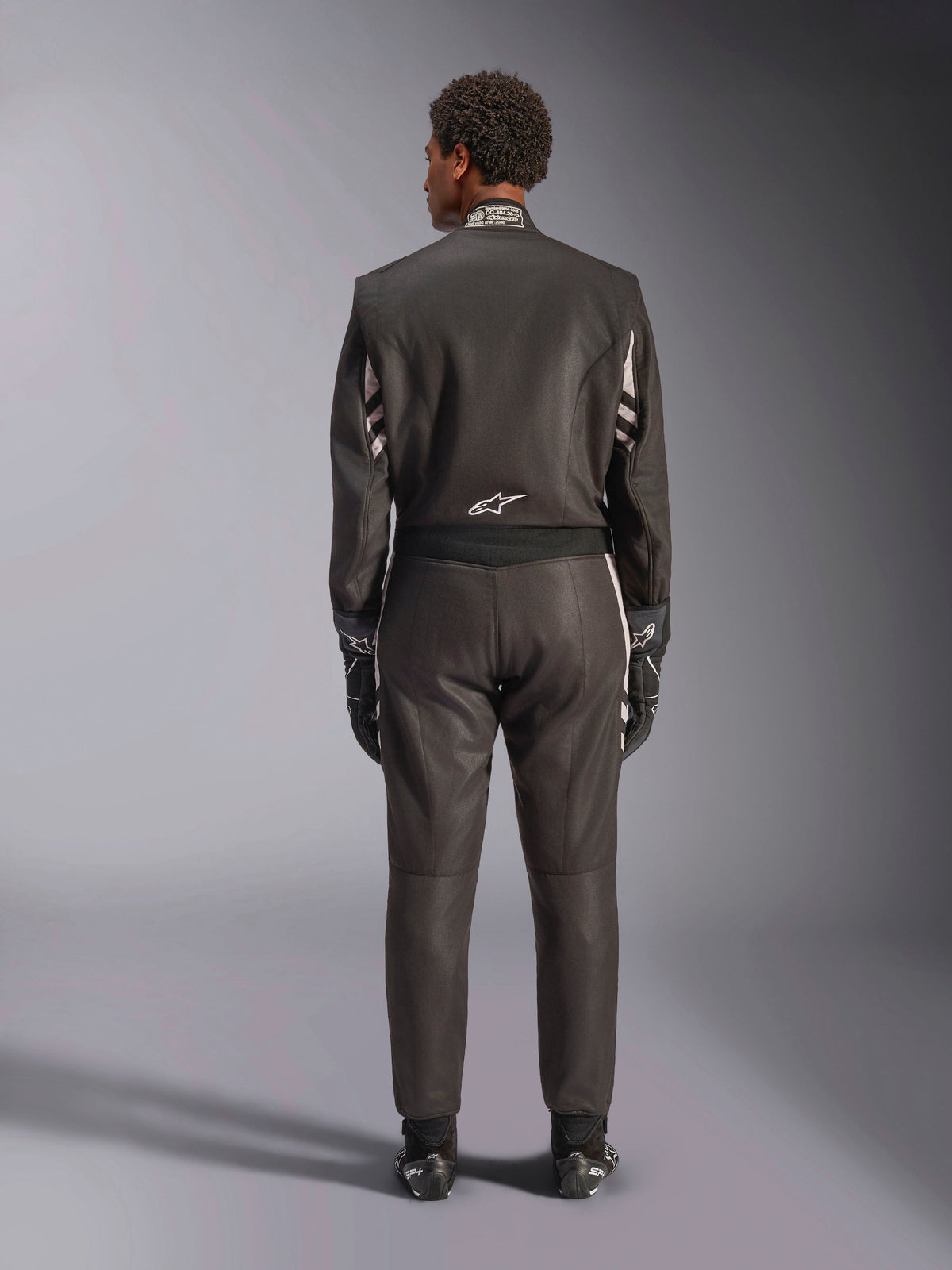 Alpinestars GP Race V3 Suit FIA, Rear View, Black and Silver, professional auto racing suit featuring two-layer aramidic construction and stretch panels, worn with matching racing gloves and boots