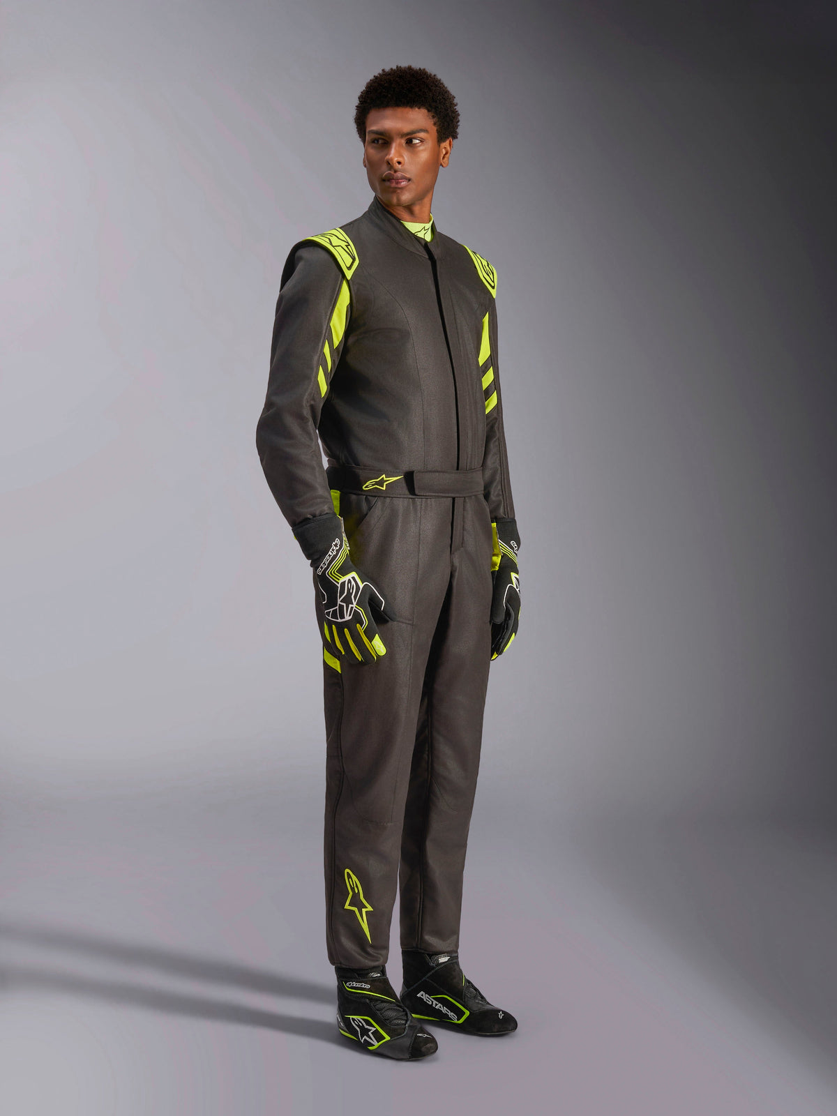 Alpinestars GP Race V3 Køredragt FIA, bilvæddeløbsdragt, sort og neongul, båret af en model med matchende racerhandsker og støvler, med markante gule detaljer på skuldre og ben, professionelt motorsportudstyr