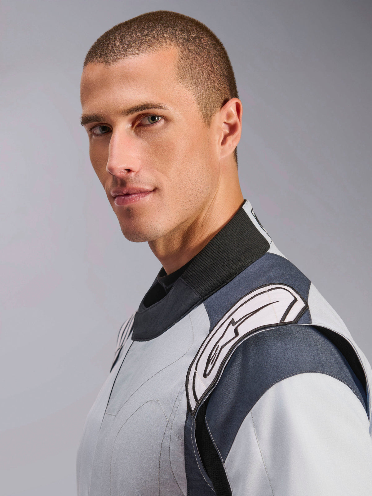 Alpinestars GP Pro Comp V2 FIA køredragt, professionel autoracerdragt til herrer, sølvblå og sort, FIA-godkendt, nærbillede af mandlig model med hvidt skulderlogo.