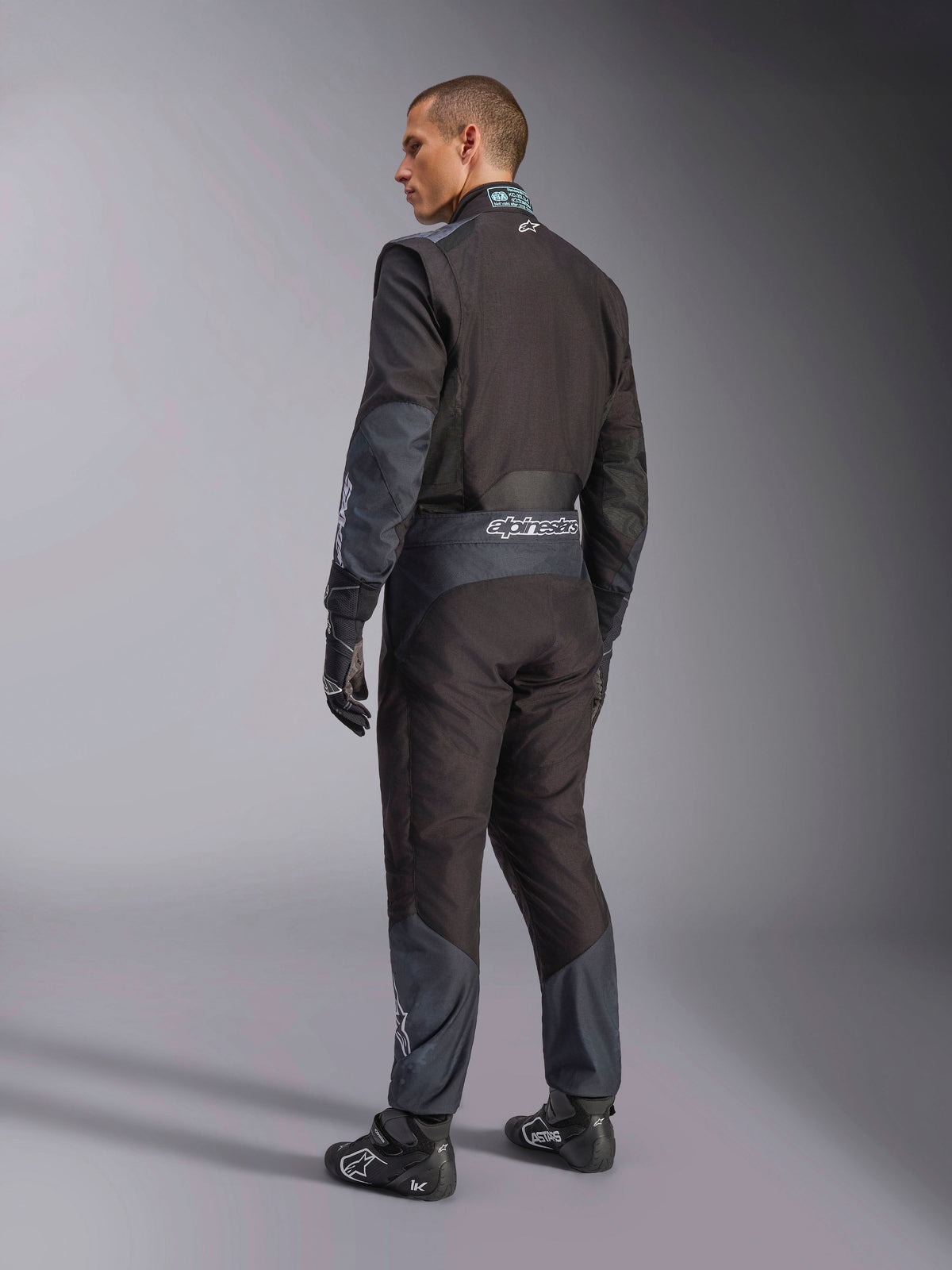 Alpinestars KMX-5 V3-dragt i Black Dark Shadow, set bagfra af model iført komplet kartingudstyr inklusiv matchende handsker og racersko, Alpinestars-branding på taljen og dark shadow-detaljer, professionelt kartingudstyr.