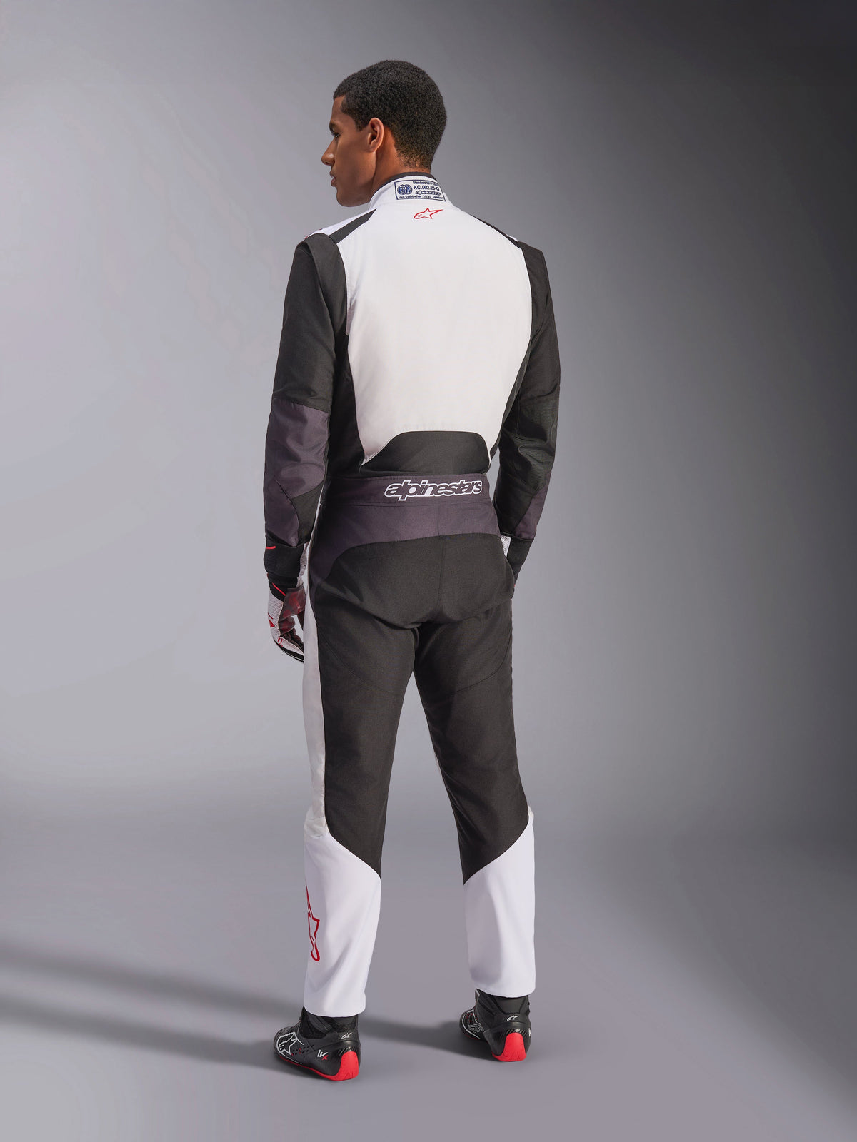 Alpinestars KMX-5 V3-dragt, kartingdragt, hvid, sort og klar rød, set bagfra af en mand iført en racerheldragt med hvid øvre ryg og sorte paneler, lille rødt logo på kraven, professionelle racestøvler og handsker