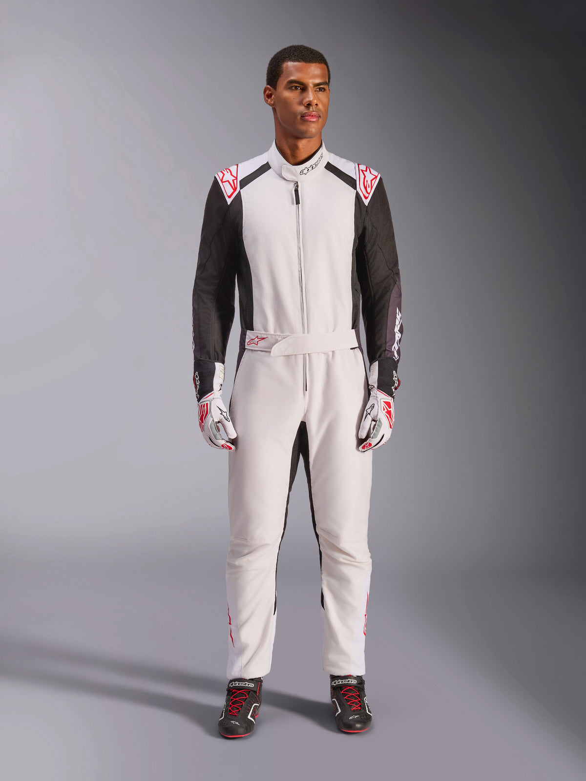 Alpinestars KMX-5 V3 køredragt, heldragt til karting, hvid, sort og lys rød, båret af en model med matchende racerhandsker og sko, professionelt motorsportudstyr til konkurrencepræget gokart-kørsel.