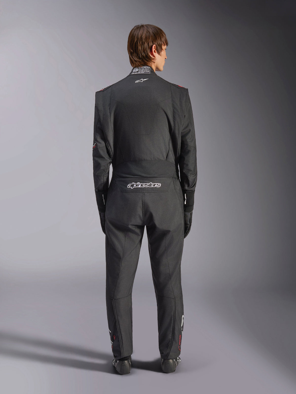 Alpinestars GP Tech V4 køredragt, auto racerdragt, sort og hvid, set bagfra med hvidt Alpinestars-branding og FIA-certificering på kraven, strømlinet ergonomisk pasform til professionel førerbeskyttelse