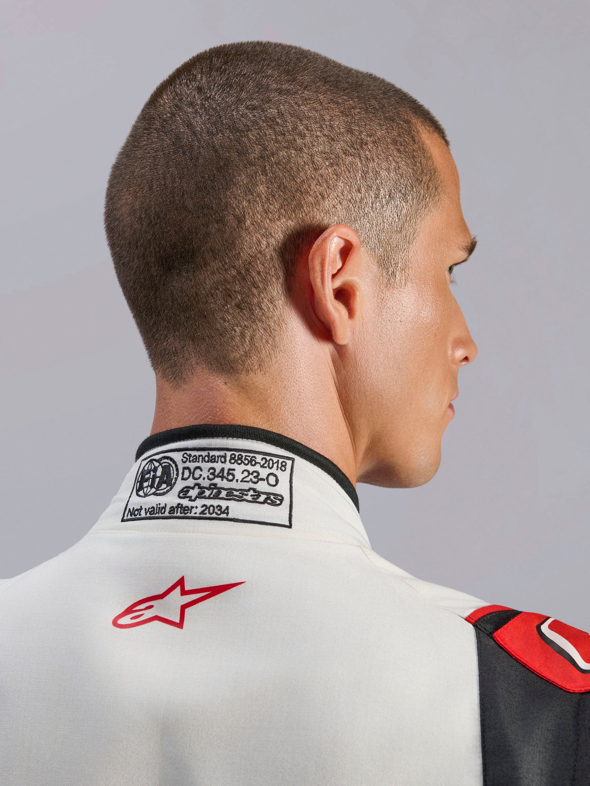Alpinestars GP Tech V4-dragt, hvid, sort og rød køredragt til bilsport, nærbillede af bagkraven med FIA 8856-2018-certificeringsmærkatet og det røde stjernelogo, professionelt sikkerhedsudstyr til motorsport