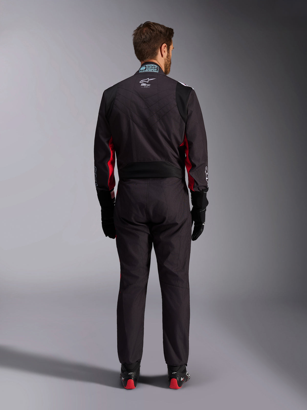 Alpinestars KMX-9 V3 Graphic 3 køredragt, kartingdragt, sort og rød, set bagfra med lændens strækpanel og FIA-certificeringsmærke på kraven, stylet med sorte racerhandsker og støvler med røde detaljer