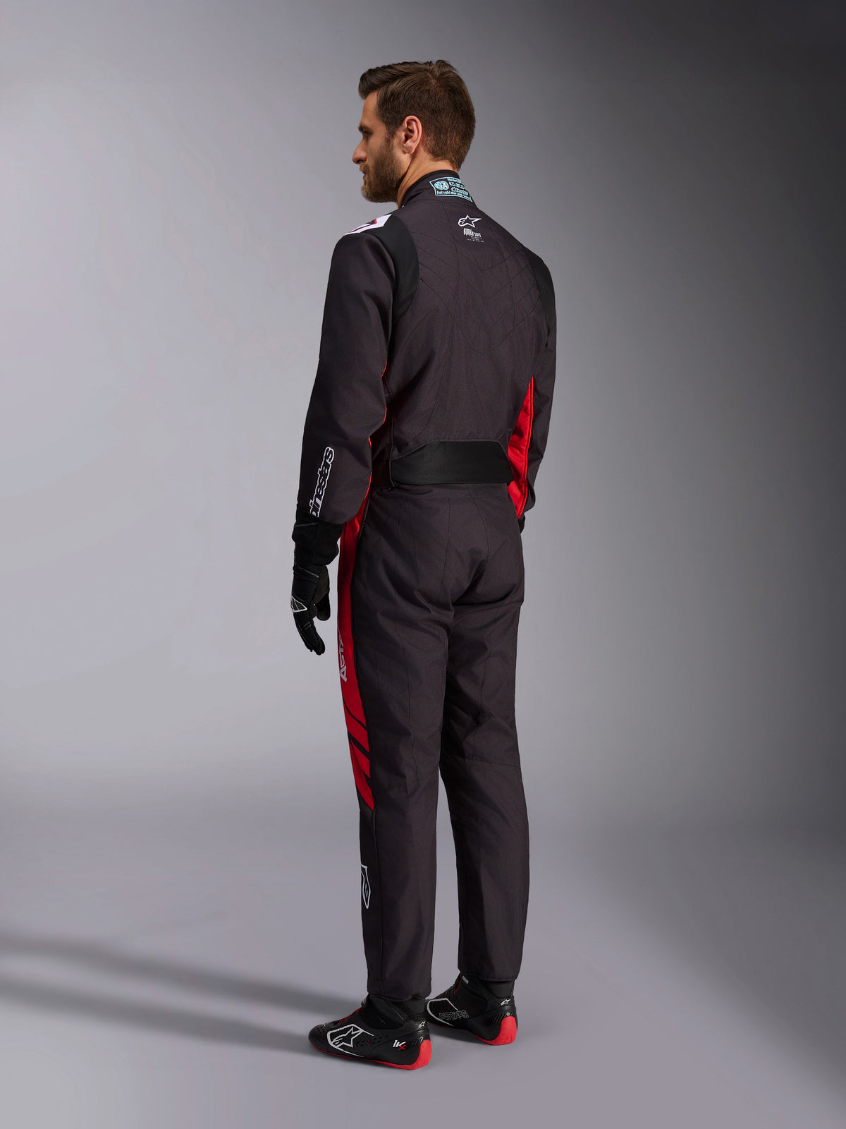 Alpinestars KMX-9 V3 Graphic 3 køredragt, sort og rød, set bagfra af model iført fuldt karting-udstyr inklusiv sorte handsker og racingstøvler, med røde sidepaneler og hvide logodetaljer