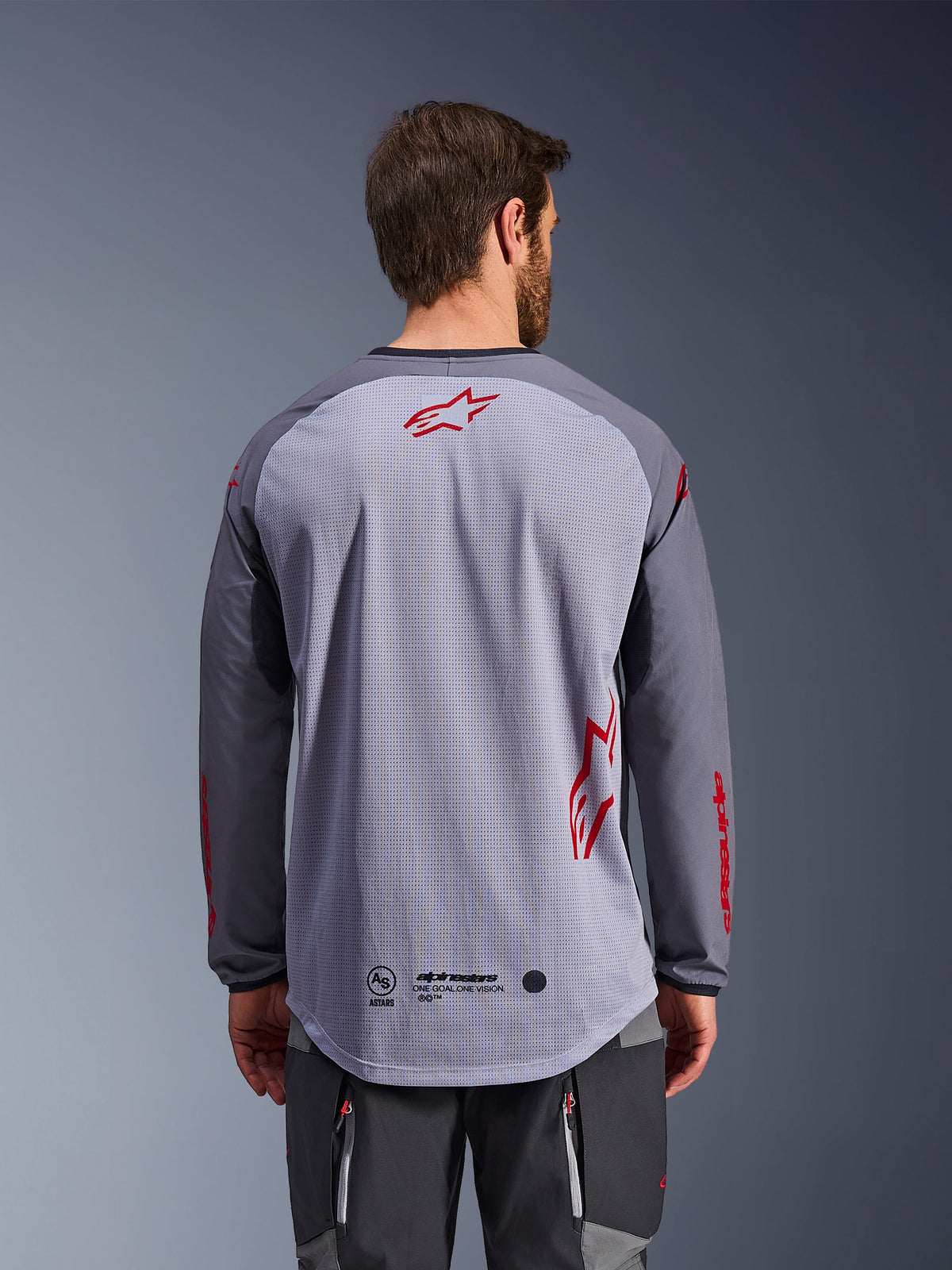 Alpinestars Maxdura Dual Jersey, set bagfra, mellemgrå og mørkegrå, åndbar mesh-ryg med røde Alpinestars-stjernelogoer, lange ærmer og forlænget drop-tail bagkant, adventure motorcykeludstyr