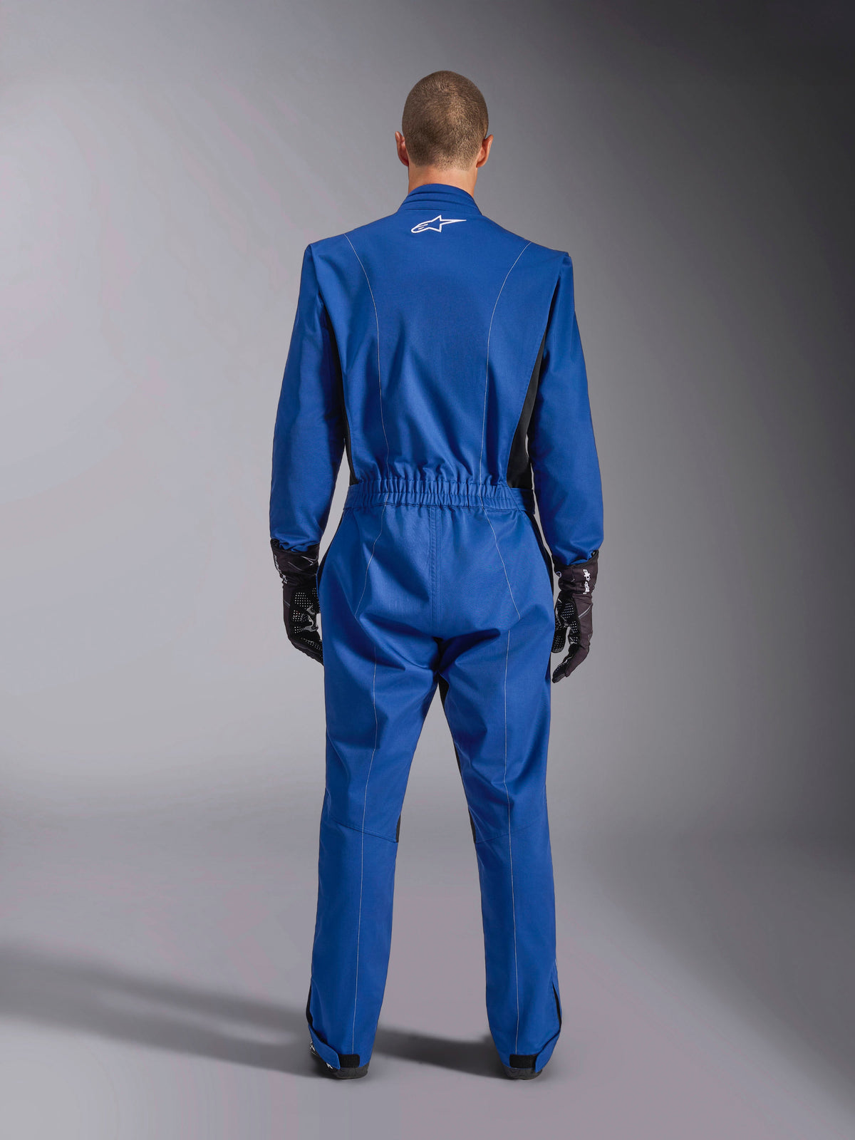 Alpinestars Kart Indoor V2 Suit, blå, set bagfra, karting-heldragt med hvidt logo på den øverste del af ryggen, elastik i taljen og sorte detaljer, båret med sorte racinghandsker