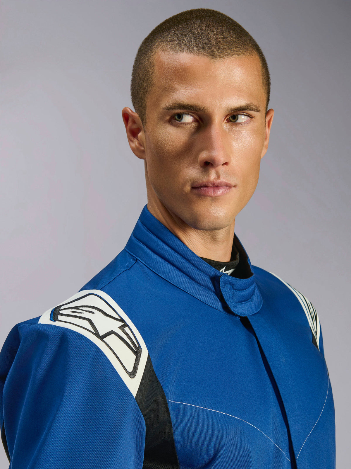 Alpinestars Kart Indoor V2 Suit, blå kartingdragt, nærbillede af mandlig model, hvide skulderpaneler med sort stjernelogo, ergonomisk krave, slidstærk enkeltlags twill til rekreativ racing