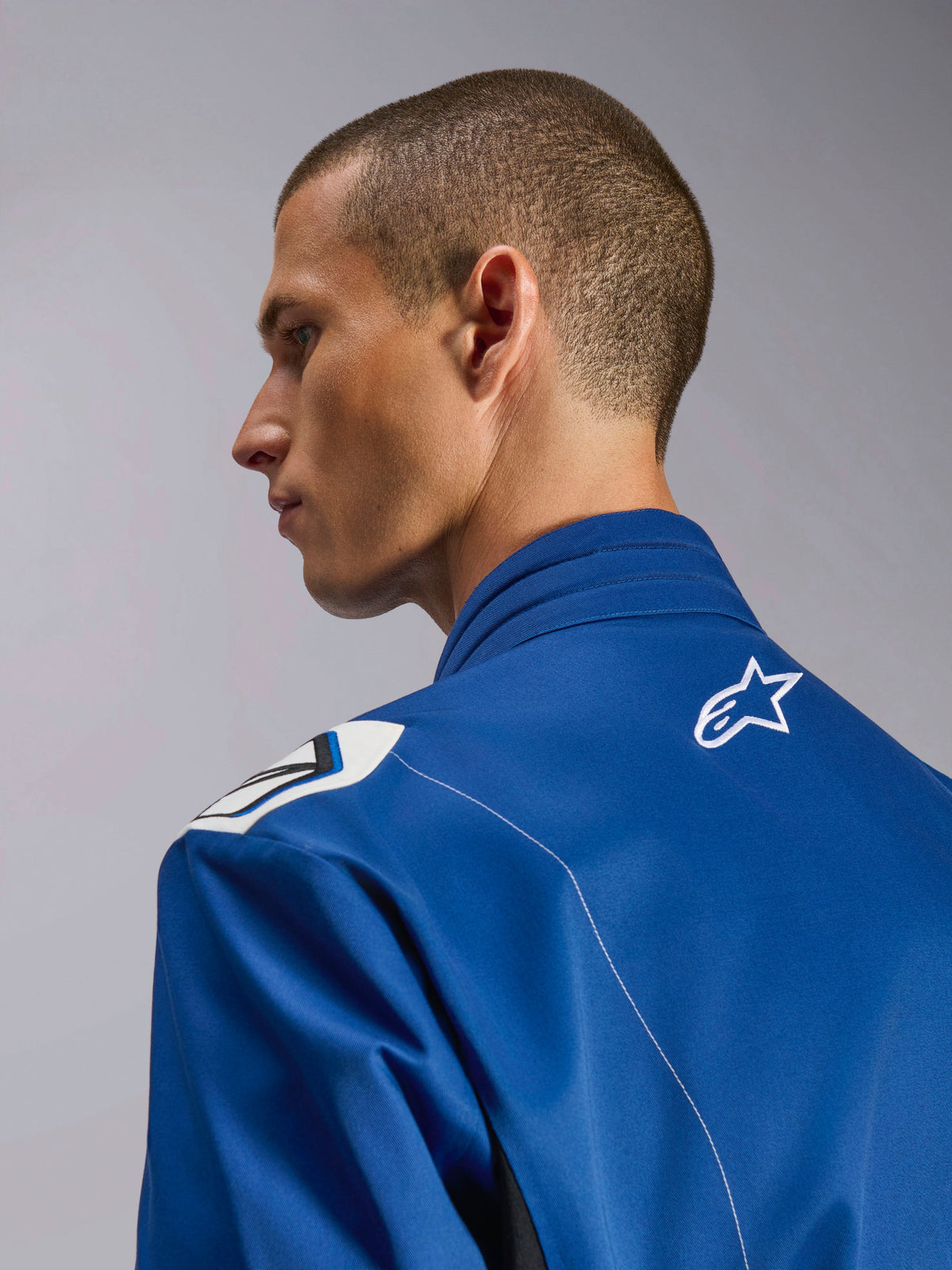 Alpinestars Kart Indoor V2 Suit, blå kartingdragt, nærbillede i sideprofil af den ergonomiske krave og øvre ryg med hvidt stjernelogo, Formel 1-inspireret skulderdesign og slidstærk poly-bomuldstwill-konstruktion