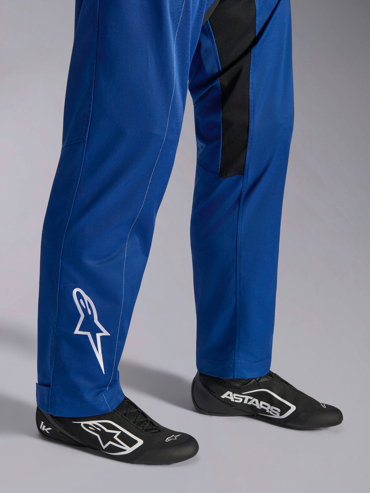 Alpinestars Kart Indoor V2 Suit, blå, nærbillede af underben og fødder med hvidt stjernelogo på anklen, justerbare benafslutninger og sorte racersko, holdbart karting-tøj til rekreativ brug på banen