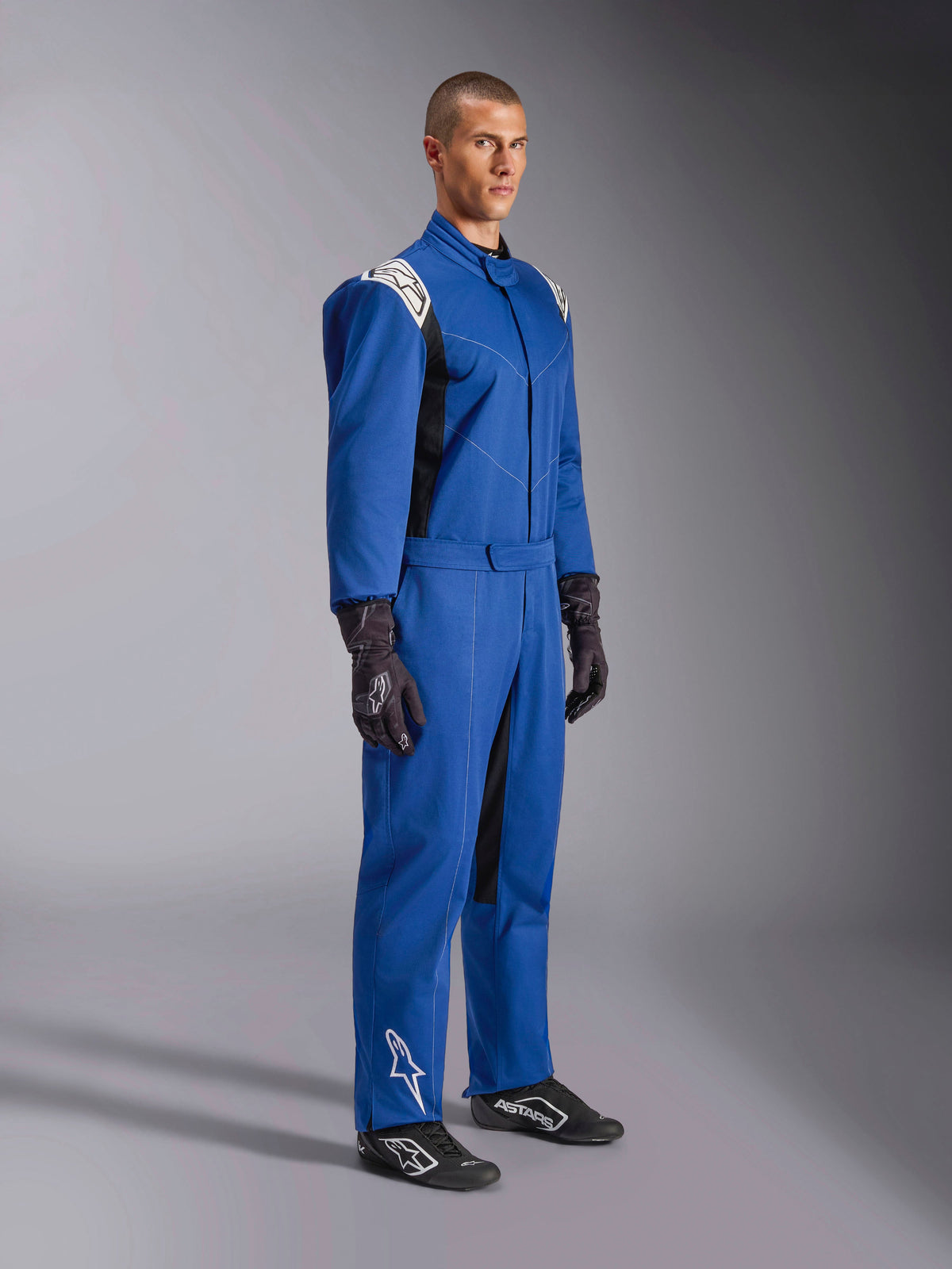 Alpinestars Kart Indoor V2 Suit, blå kartingdragt, racing-overall med hvide skulderpaneler og logoer, justerbart taljebælte, hvidt logo på underbenet, båret af model med sorte racinghandsker og sko, motorsportsbeklædning til indendørs karting