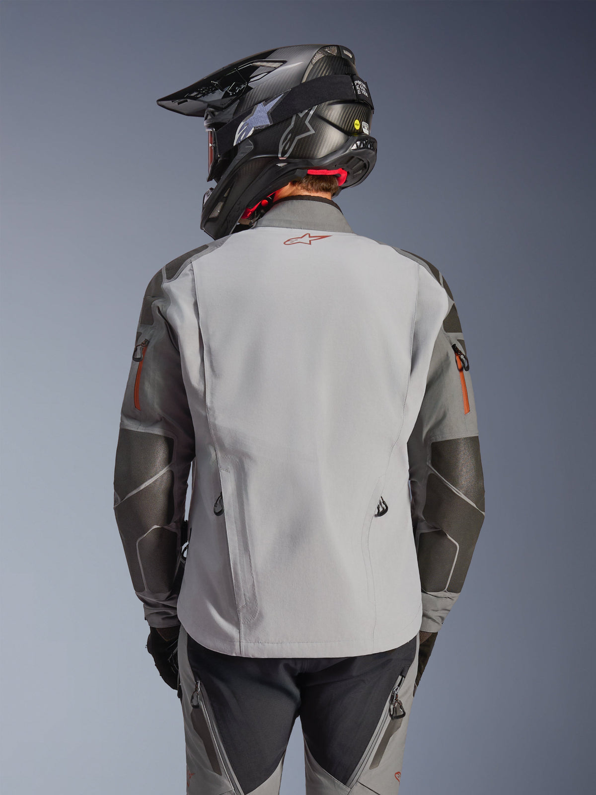 Alpinestars Nazca 3L GORE-TEX PRO-jakke, adventure-motorcykeljakke, set bagfra, mørkegrå og mellemgrå, Superfabric-forstærkninger på albuer og skuldre, rødt logo på ryggen, båret med matchende adventure-udstyr og en kulfiberhjelm
