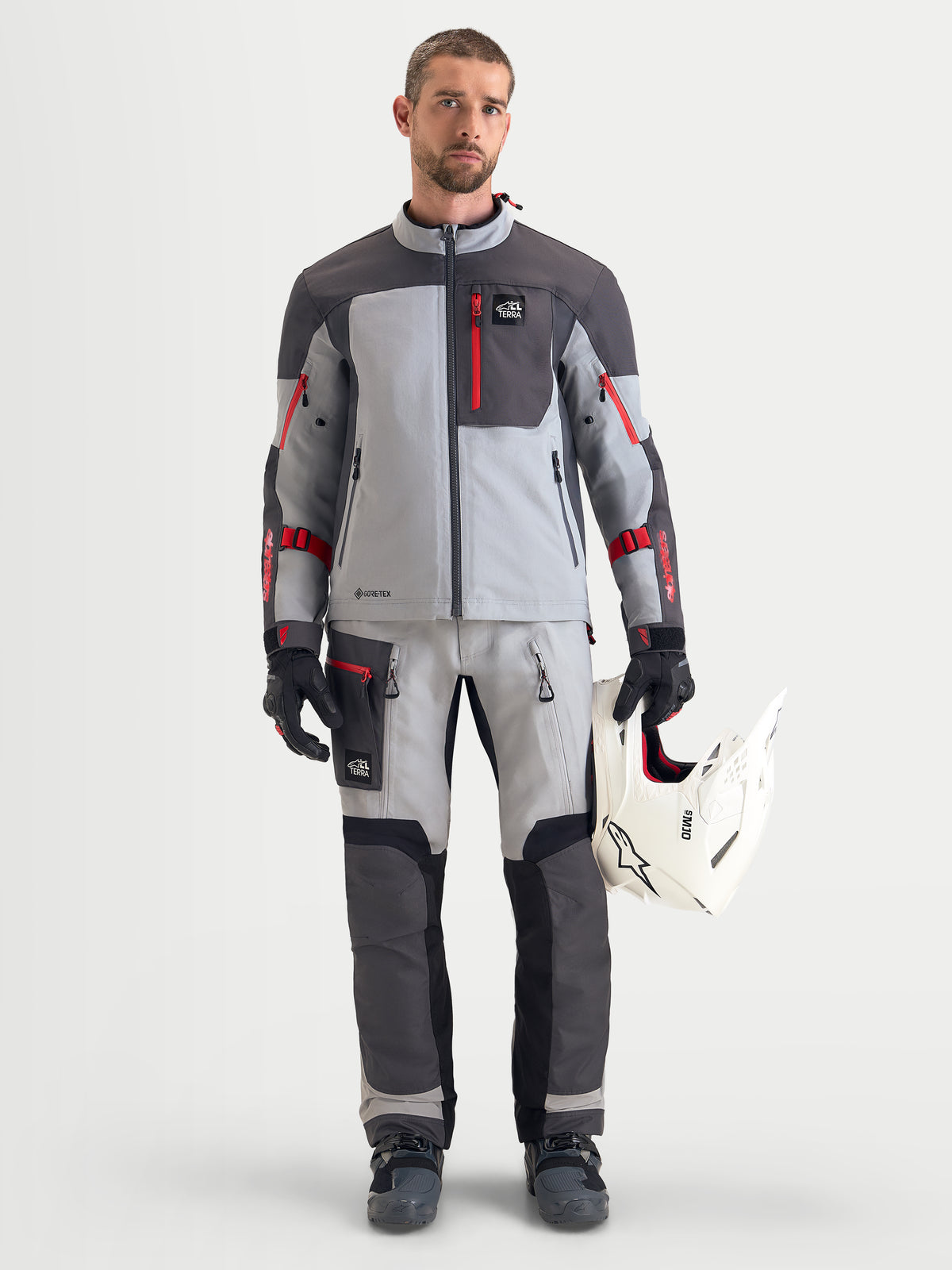 Alpinestars Arenis Gore-Tex udstyrssæt, herre adventure-motorcykeljakke og -bukser i grå og mørkegrå med røde detaljer, set forfra på model iført matchende køredragt, handsker og med en hvid hjelm, vandtæt all-terrain-udstyr