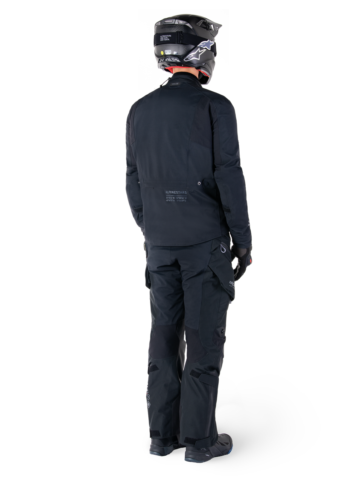 Set bagfra af en kører iført Alpinestars St-7 Prime GORE-TEX-jakke i sort, kombineret med matchende sorte touringbukser, sort motorcykelhjelm med hvidt logo og sorte motorcykelstøvler, komplet beskyttende adventure-udstyr til touring og pendling.