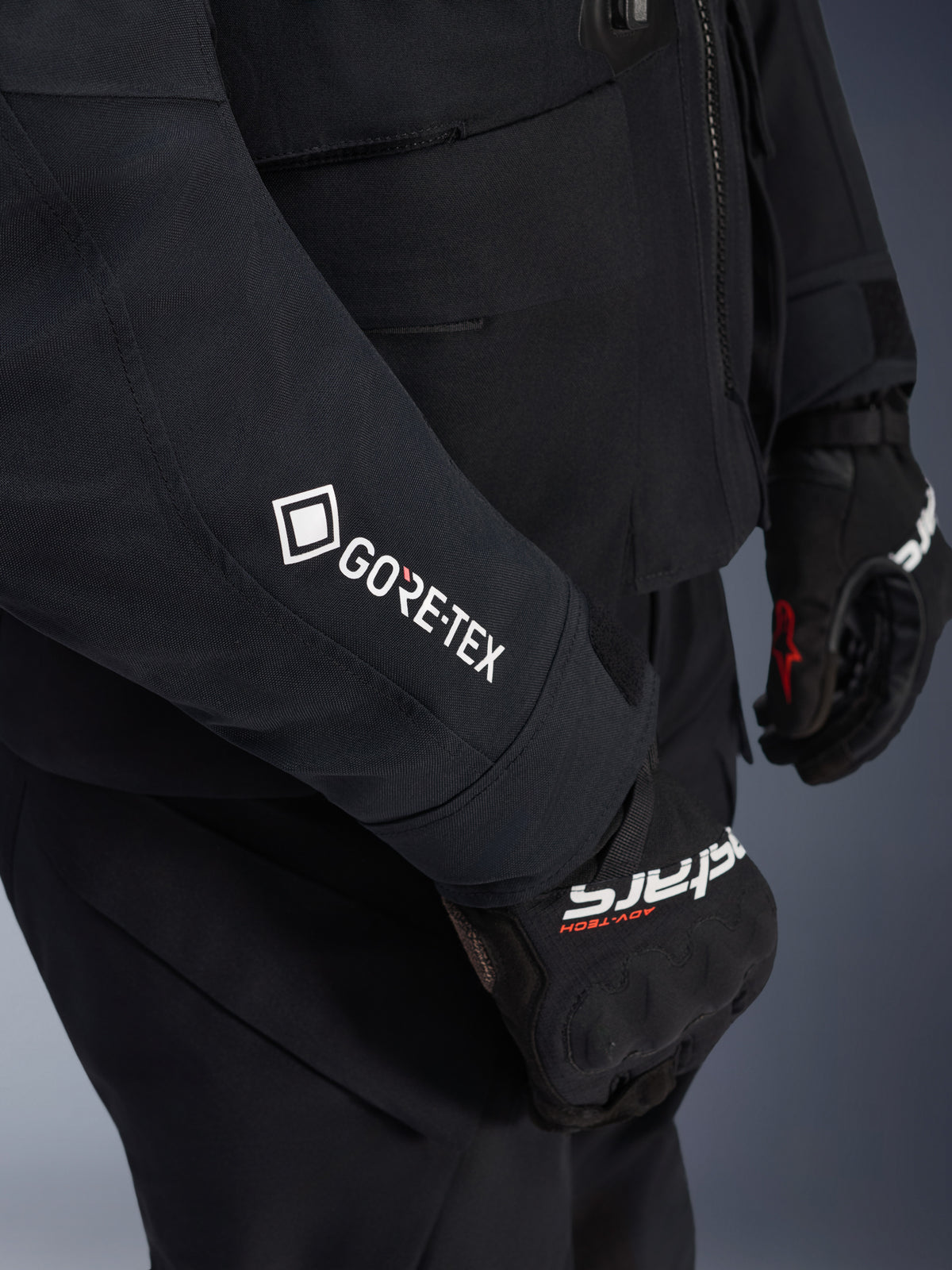 Alpinestars ST-7 2L GORE-TEX jakke, sort og mørkegrå, nærbillede af ærme med hvidt GORE-TEX-logo, båret med sorte adventure-kørehandsker, vandtæt motorcykelbeklædning