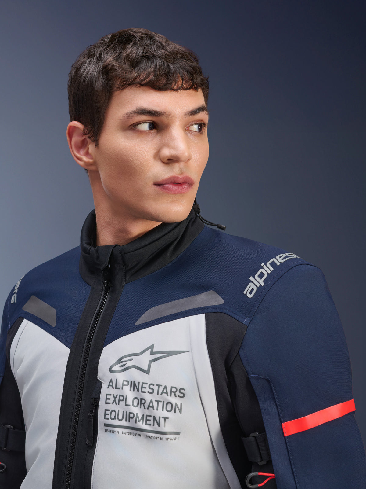 Alpinestars ST-7 2L GORE-TEX-jakke, Ice Gray, mørkeblå og sort, bæres af mandlig model, med Alpinestars Exploration Equipment-branding på brystet, høj krave og rød accent på ærmet, slidstærkt tekstildesign til adventure touring
