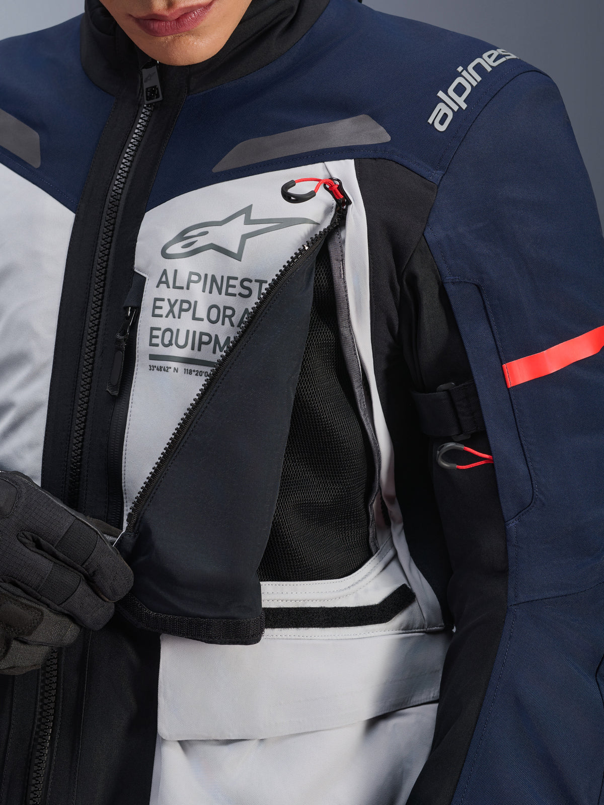 Alpinestars ST-7 2L GORE-TEX jakke, adventure touring-jakke, Ice Gray, mørkeblå og sort, detaljeret visning af det åbnede ventilationspanel på brystet, der afslører sort mesh, med Alpinestars Exploration Equipment-logo og røde detaljer på lynlåsstropperne