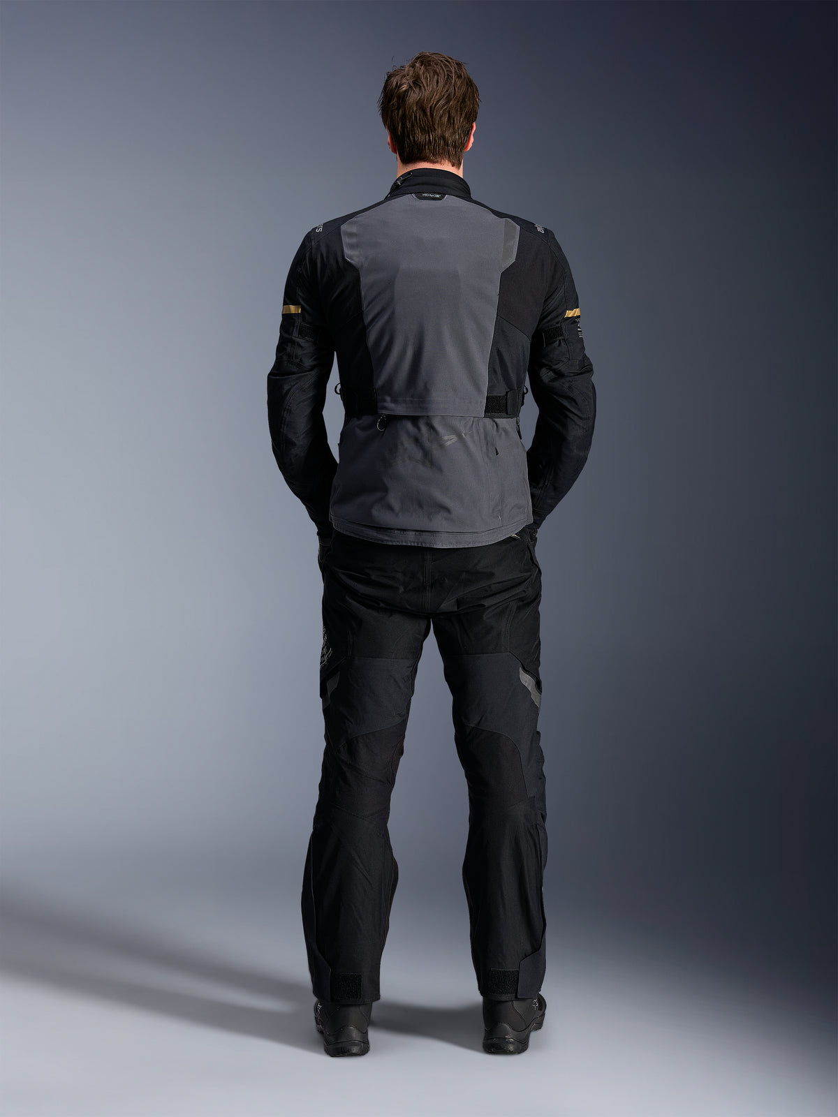 Alpinestars ST-7 2L GORE-TEX Jacket, Deep Gray Black and Dark Khaki, rear view on a model, adventure motorcycle touring jacket with gray back panel and black articulated sleeves, worn with matching black pants.