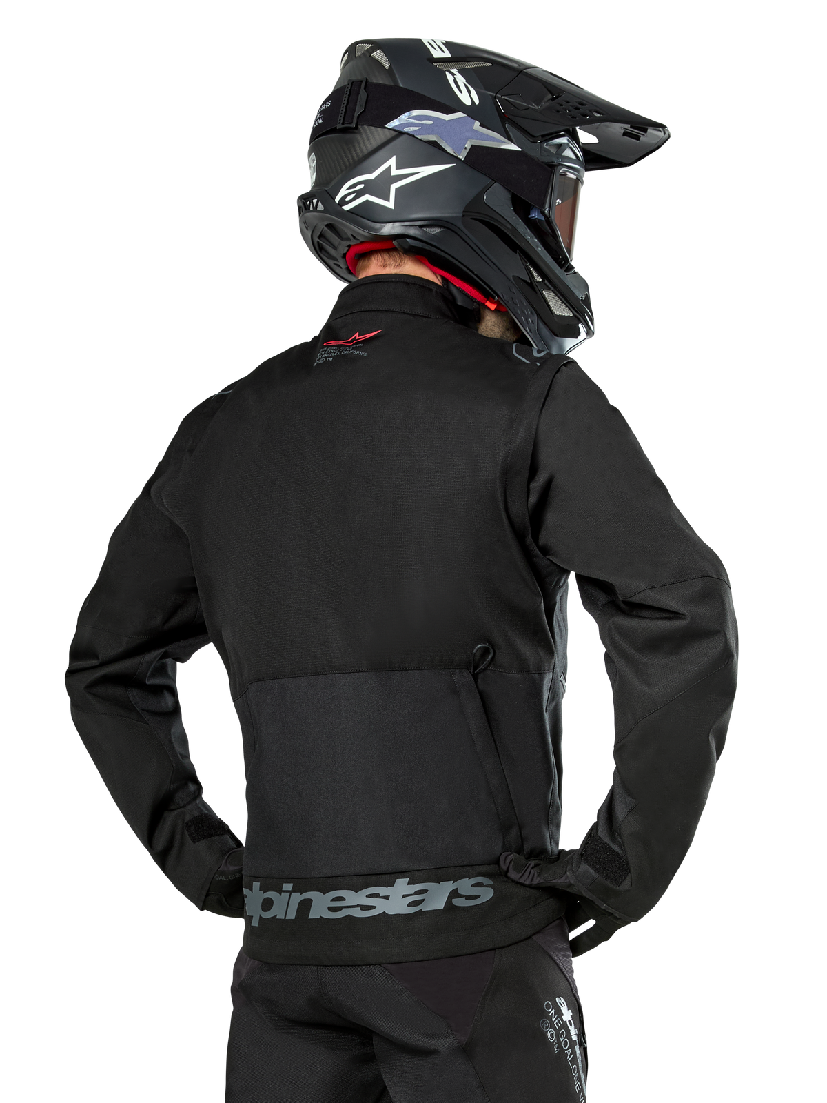 Alpinestars Pro-Dura jakke set bagfra, sort, holdbar ripstop-tekstil enduro-jakke, stor baglomme med gråt Alpinestars-branding nederst på ryggen, kombineret med en sort motocross-hjelm