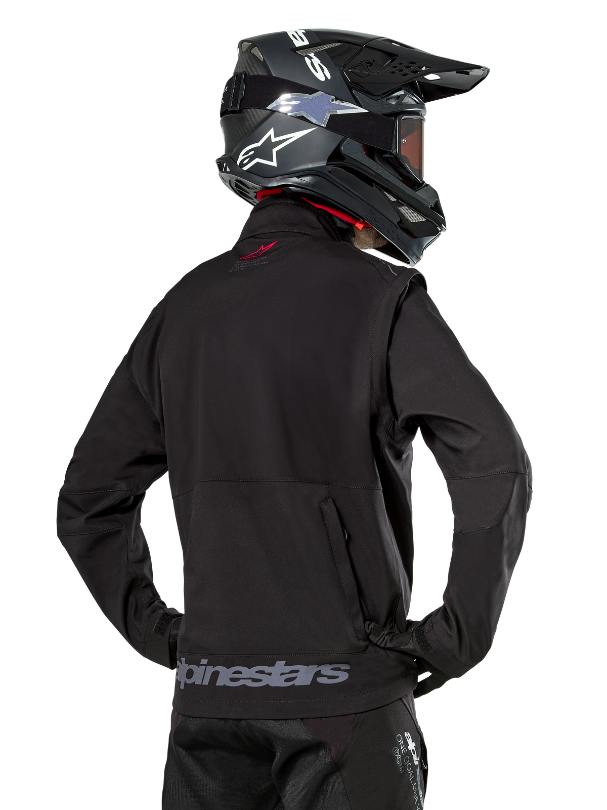 Alpinestars Lite-Dura Softshell-jakke, sort, set bagfra på en kører, med gråt Alpinestars-branding på den nederste kant bagpå og et lille rødt logo på kraven, kombineret med en sort motocross-hjelm, designet til enduro- og terrænkørsel