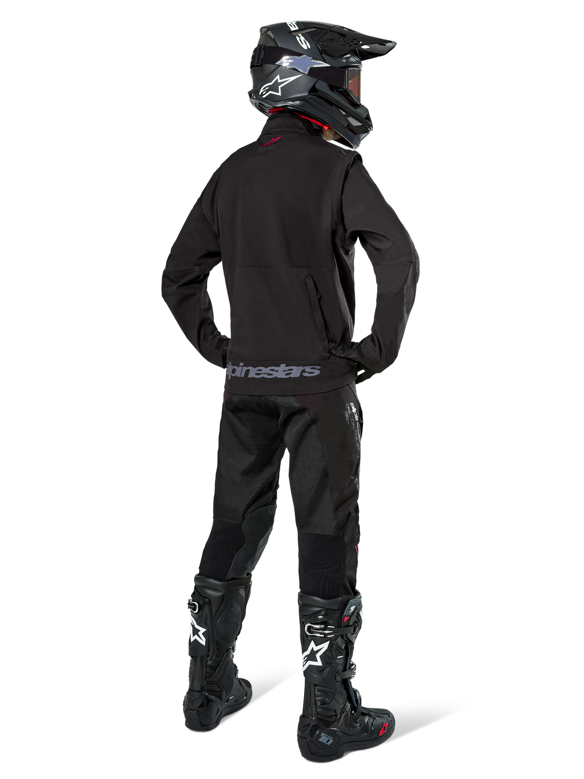 Enduro-kører set bagfra, iført Alpinestars Lite-Dura Softshell Jakke i sort, kombineret med sorte tekniske kørebukser og støvler, med en baglomme med lynlås og Alpinestars-logo på den nederste kant, komplet off-road-udstyr til motocross.