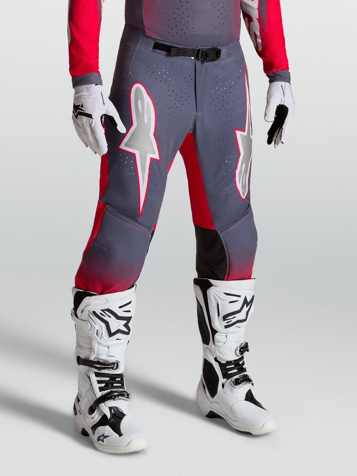 Alpinestars Supertech Hiten AFD bukser, grå og neonrøde motocrossbukser med hvid stjernegrafik og magnetisk spænde, vist med hvide MX-støvler
