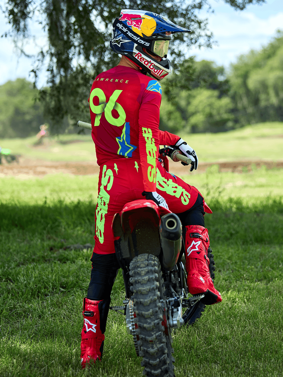 Motocrosskører siddende på en rød motocrossmaskine, Alpinestars 2025 Supertech Maker-bukser i Bright Red og Yellow Fluo, matchende rød trøje med '96' og 'LAWRENCE' på ryggen, røde racestøvler og en Red Bull-hjelm, professionelt off-road racerudstyrssæt