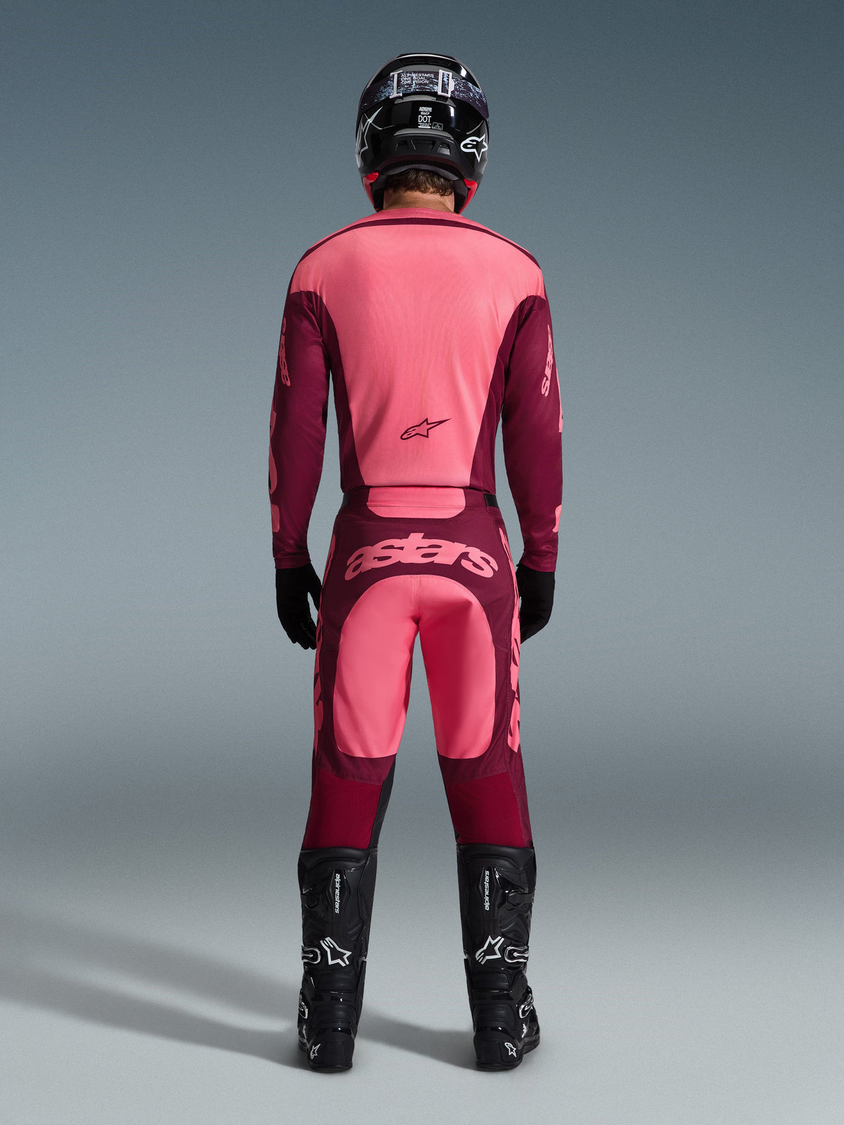 Motocrosskører set bagfra iført Alpinestars 2026 Racer Riway Jersey og matchende bukser i Dark Red Coral, med sorte støvler, en sort hjelm og sorte handsker, koordineret højpræstationsudstyr til off-road racing