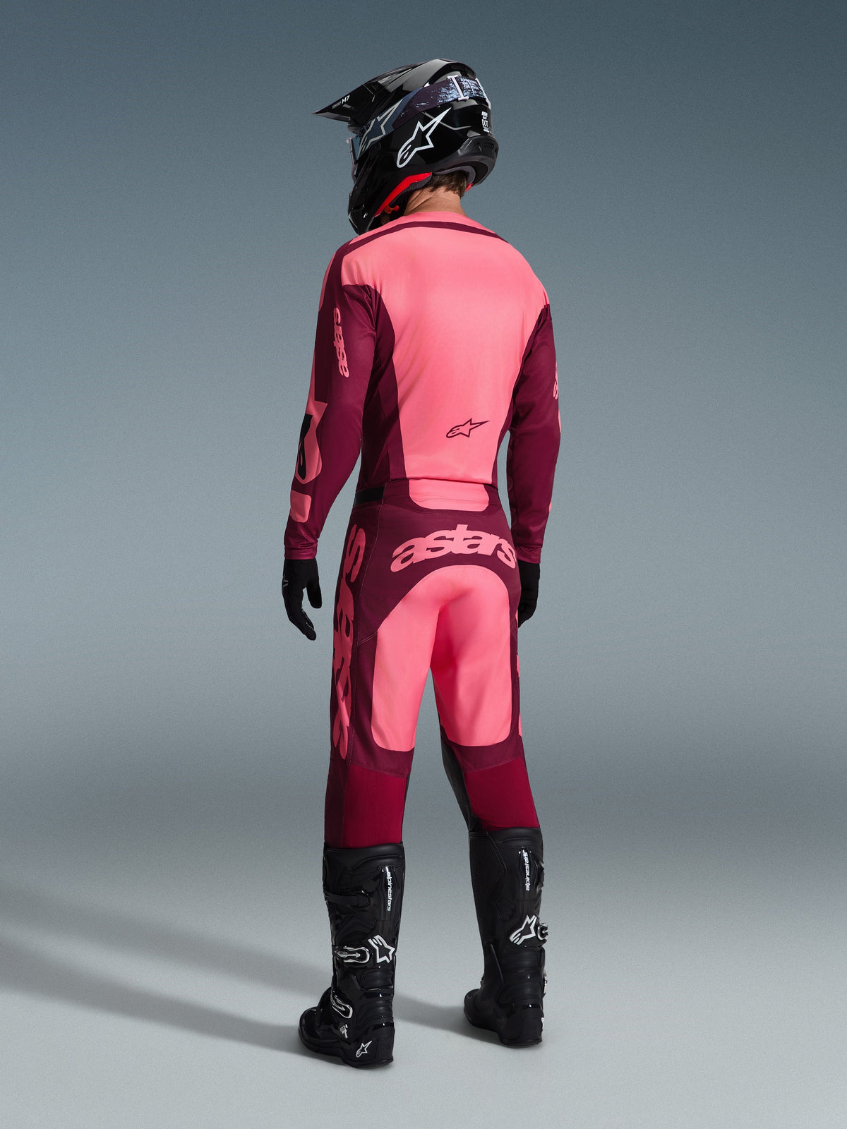 Alpinestars 2026 Race r Riway trøje og matchende bukse r, motocross-udstyr i Dar k Red Coral, se t bagfr a a f køre r me d sor t hjel m o g sort e støvler, me d livlig e kora l- o g mørkerød e panele r o g markan t Astar s-brandin g på ryggen