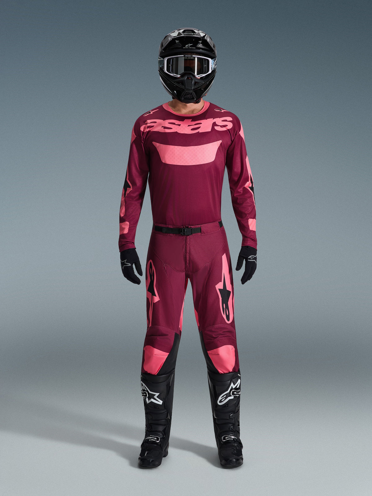 Motocrosskører iført komplet racerudstyr, 2026 Racer Riway-trøje i Dark Red Coral, matchende mørkerøde bukser med koralfarvede detaljer, sort hjelm med hvide detaljer, sorte støvler med hvide logoer og sorte handsker, koordineret sæt til off-road kørsel