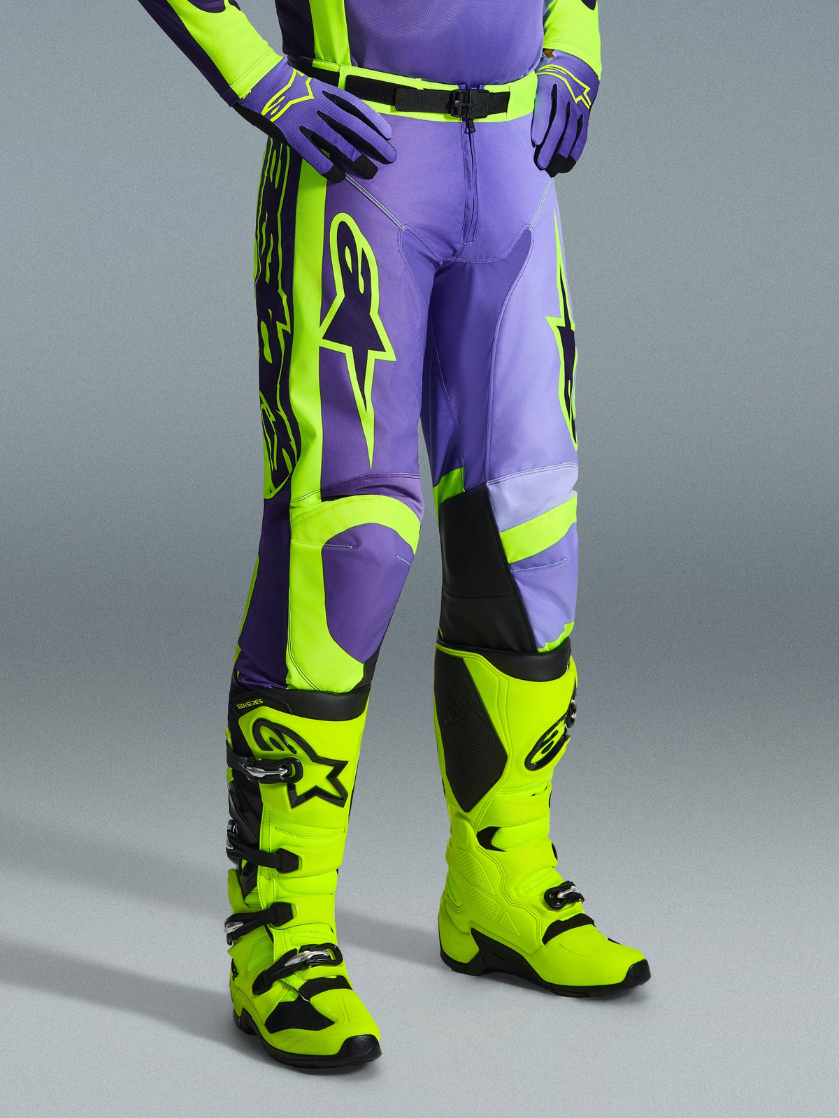 Alpinestars 2026 Racer Portl bukser, motocross-bukser i lilla og gul fluo, båret af en kører med matchende fluo-gule støvler og lilla handsker, med markant Alpinestars-branding og ergonomisk design til off-road ydeevne